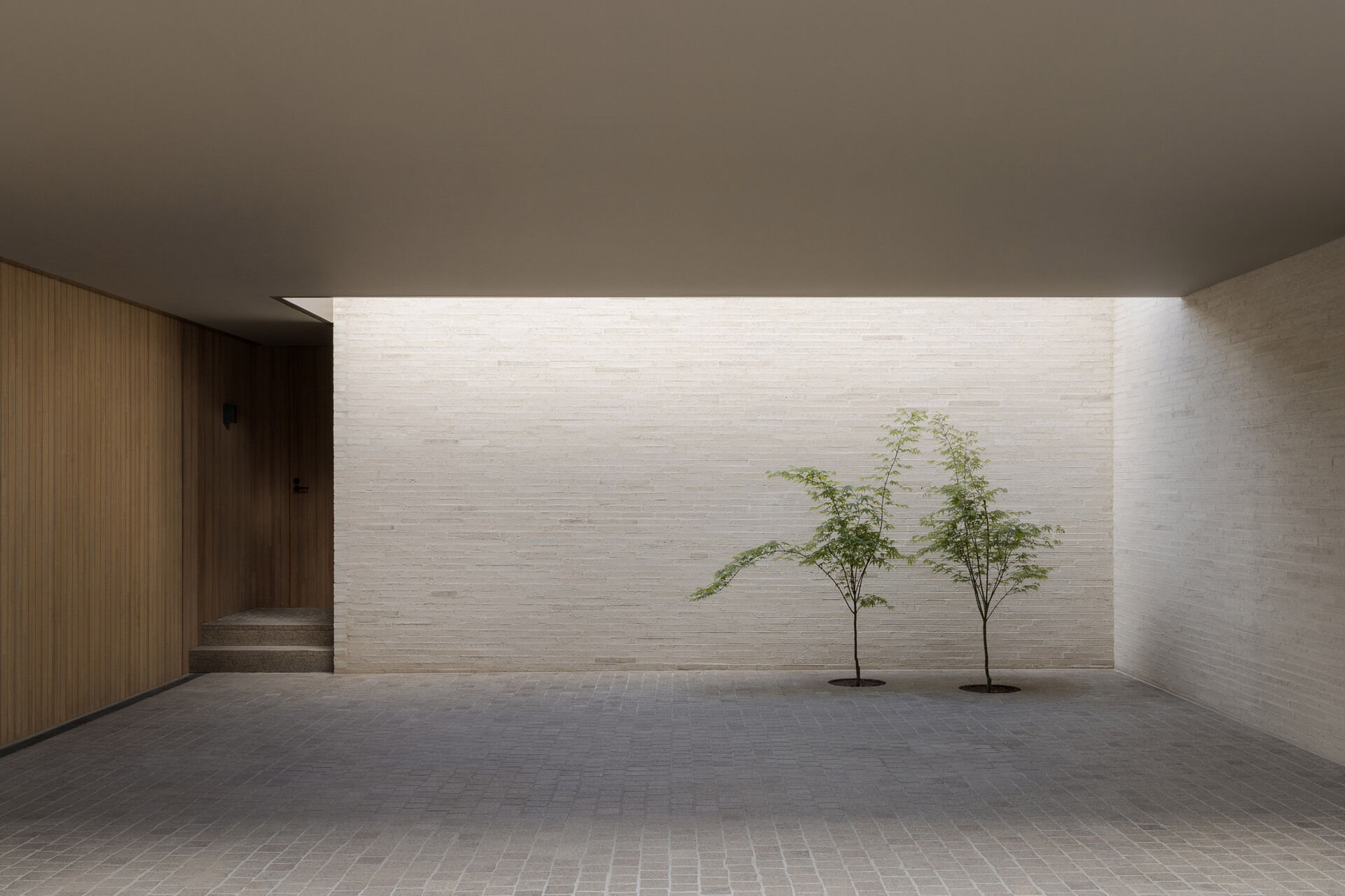 The exterior is defined by white brick, used across a facade with very few openings. From the laneway, the building appears solid and quiet. Behind that exterior, the architecture becomes increasingly layered, balancing rational planning with brick, timber, travertine, planting, textiles, art and collected objects.