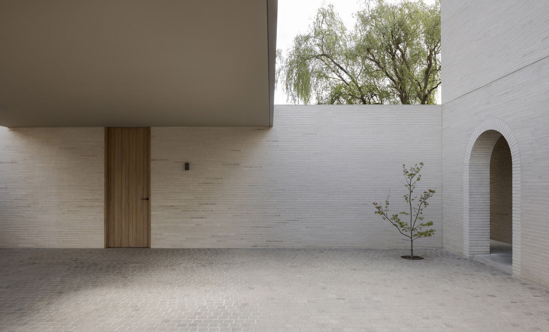 The exterior is defined by white brick, used across a facade with very few openings. From the laneway, the building appears solid and quiet. Behind that exterior, the architecture becomes increasingly layered, balancing rational planning with brick, timber, travertine, planting, textiles, art and collected objects.