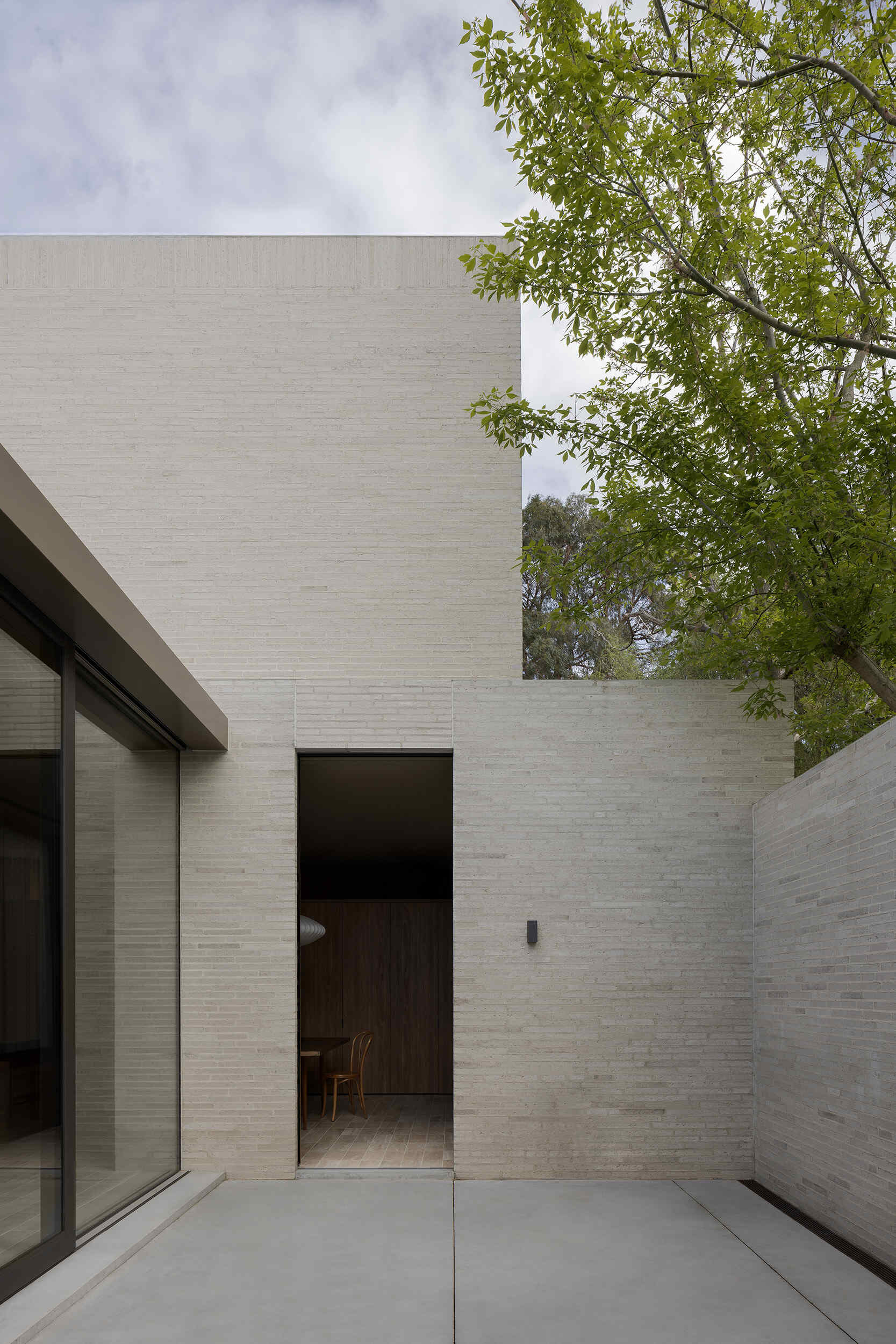 Warm timber cabinetry, bentwood chairs, a dark dining table and an oversized white pendant define Casa Piva’s dining area, with the larger internal courtyard bringing daylight and planting into the living spaces.