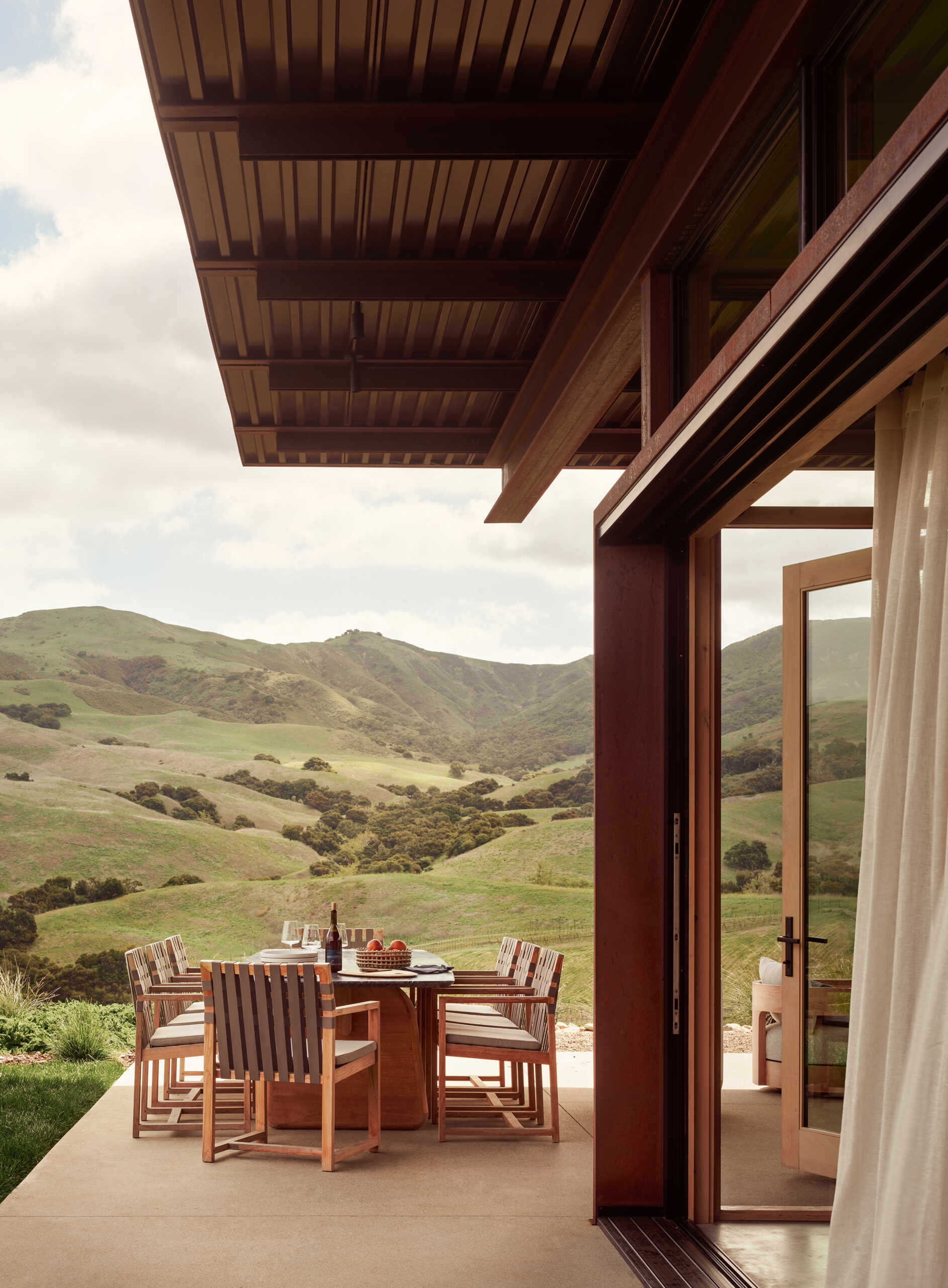 A generous covered terrace and outdoor fireplace extend the living spaces of this California vineyard residence outdoors, framing panoramic views of the surrounding hillside.