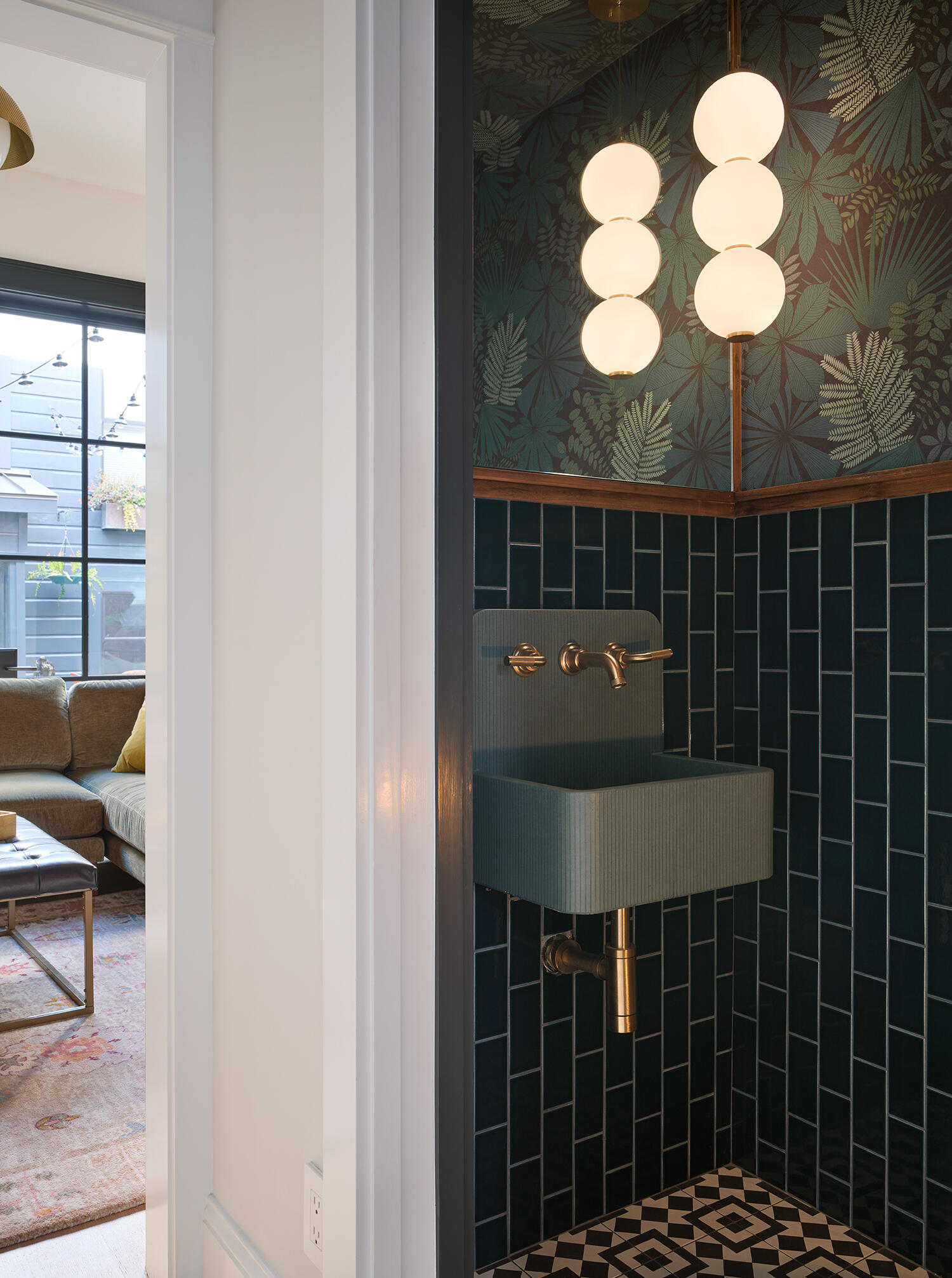 Deep green tile, botanical wallpaper, warm brass fixtures and a patterned floor give this compact San Francisco powder room a rich, layered look with plenty of personality.