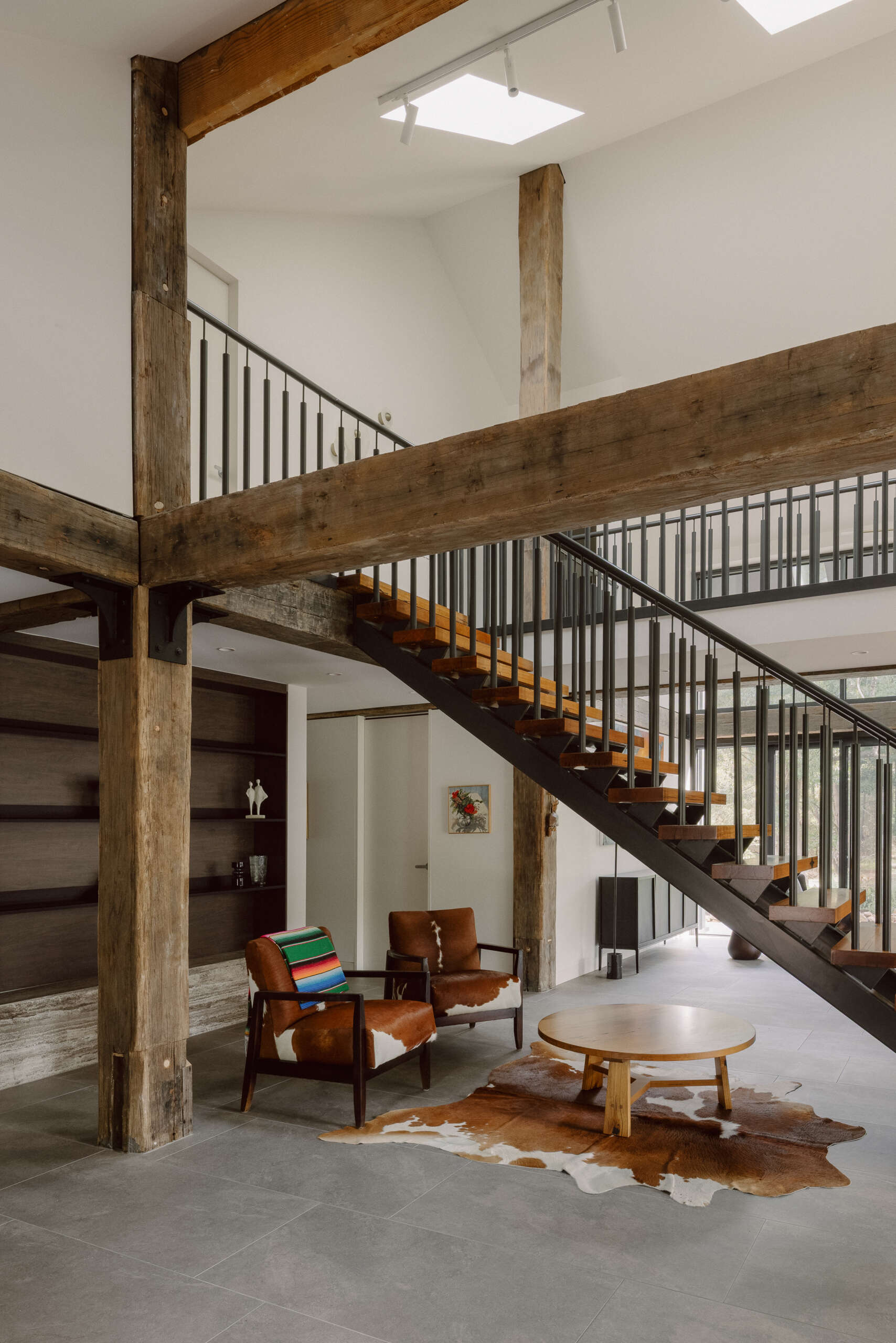 Tour the staircase and sitting area at Yarra Valley House, featuring timber and metal details, exposed beams, cowhide armchairs and a cosy space beneath the stairs.
