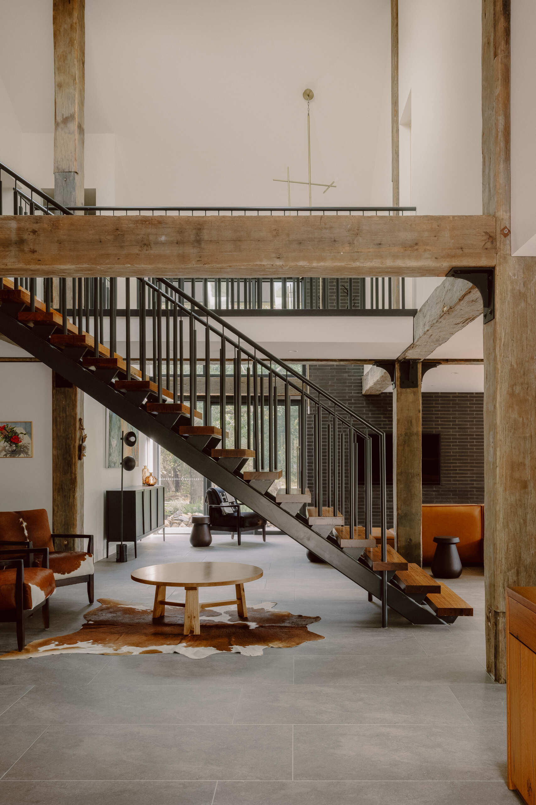 Tour the staircase and sitting area at Yarra Valley House, featuring timber and metal details, exposed beams, cowhide armchairs and a cosy space beneath the stairs.