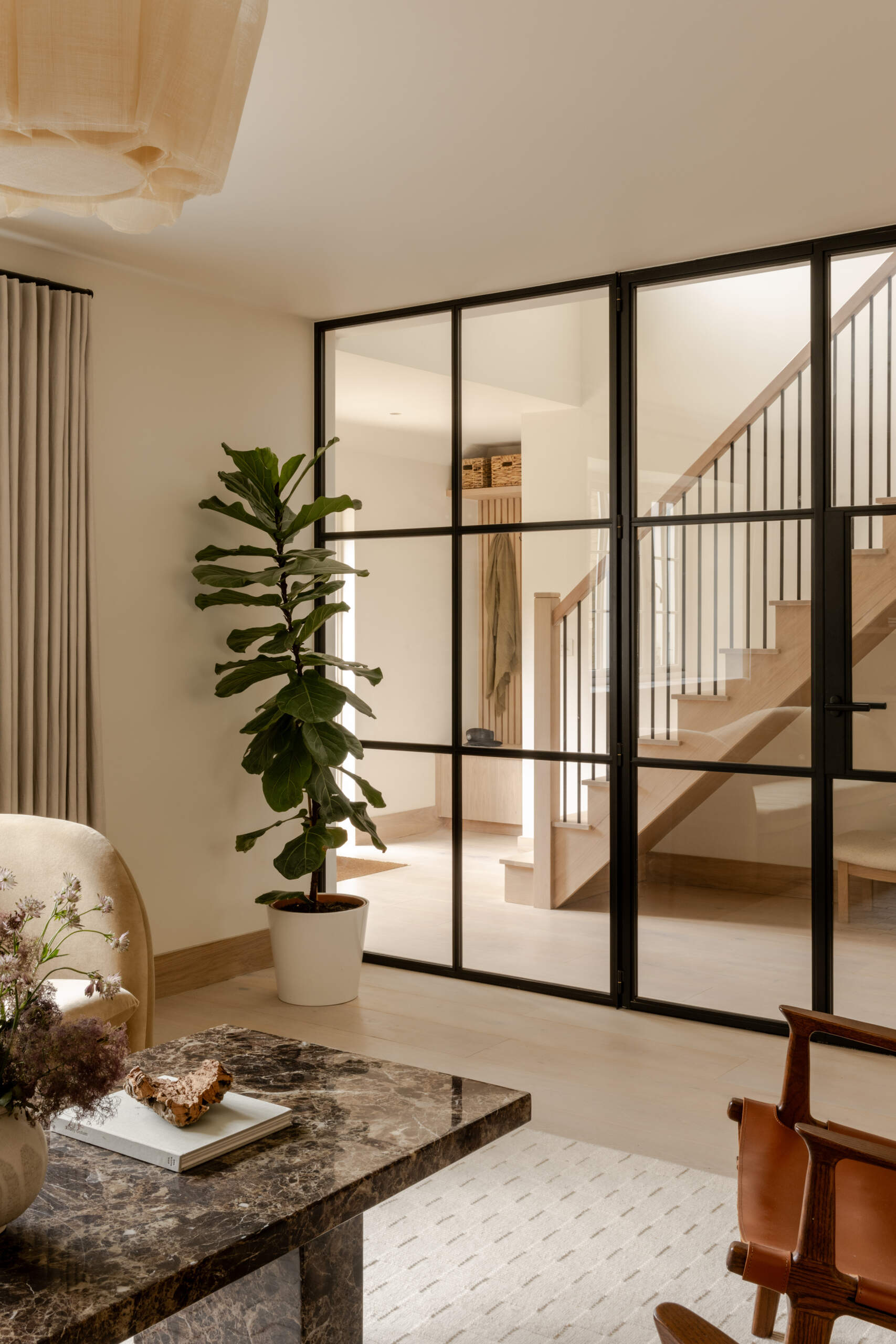 Explore the sitting room at Thirsk Cottage, where a black-framed glass wall, pale wood, warm leather and a dark fireplace create a comfortable balance of modern and natural materials.