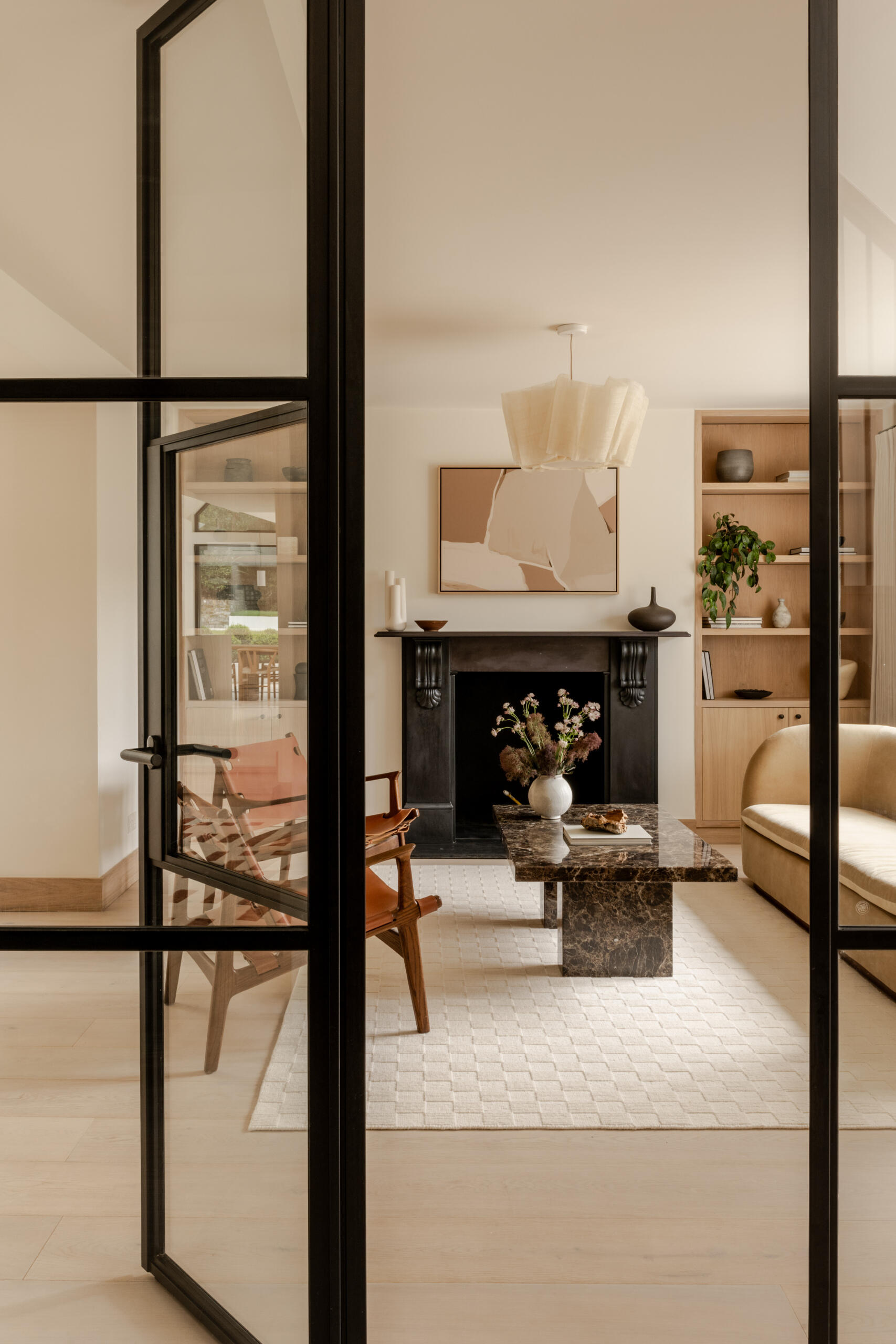 Explore the sitting room at Thirsk Cottage, where a black-framed glass wall, pale wood, warm leather and a dark fireplace create a comfortable balance of modern and natural materials.