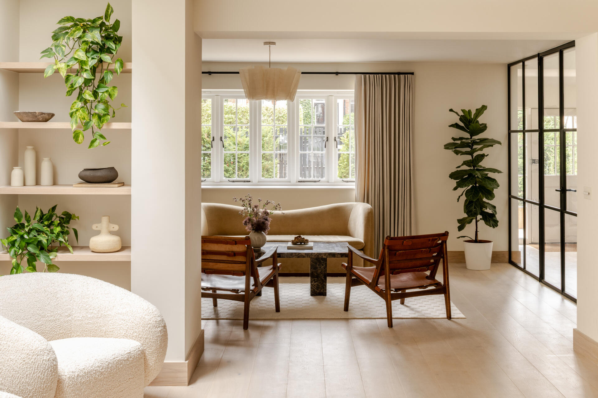Explore the sitting room at Thirsk Cottage, where a black-framed glass wall, pale wood, warm leather and a dark fireplace create a comfortable balance of modern and natural materials.