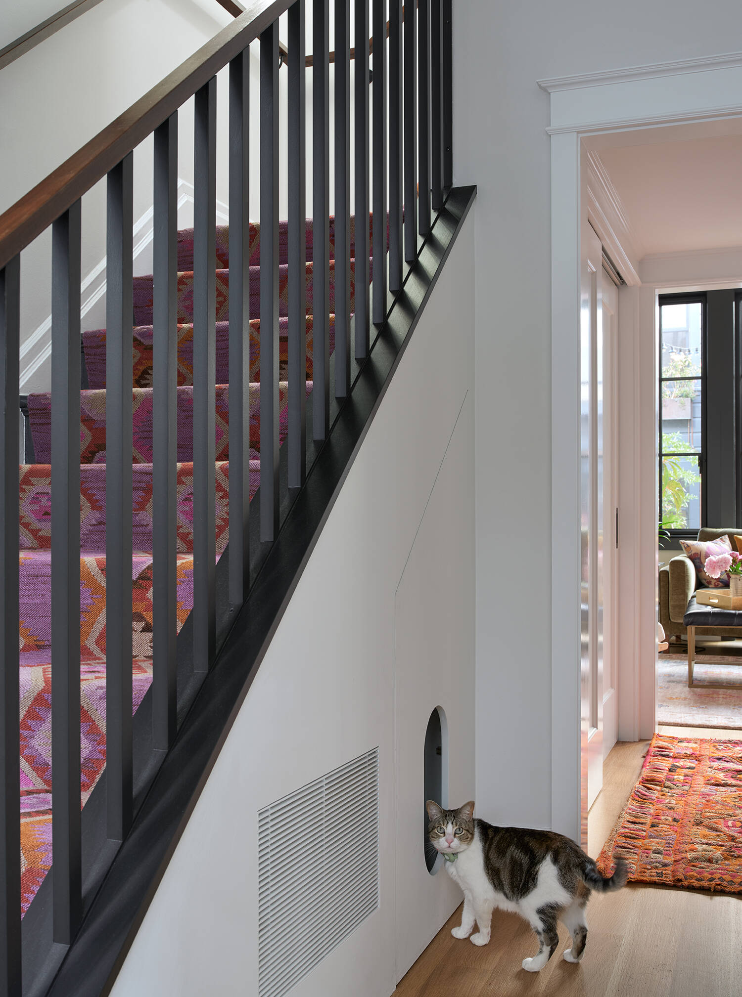 A bold patterned stair runner, black balusters and dark wood handrail bring colour and character to this crisp white stairwell, complete with a charming arched cat door beneath the stairs.