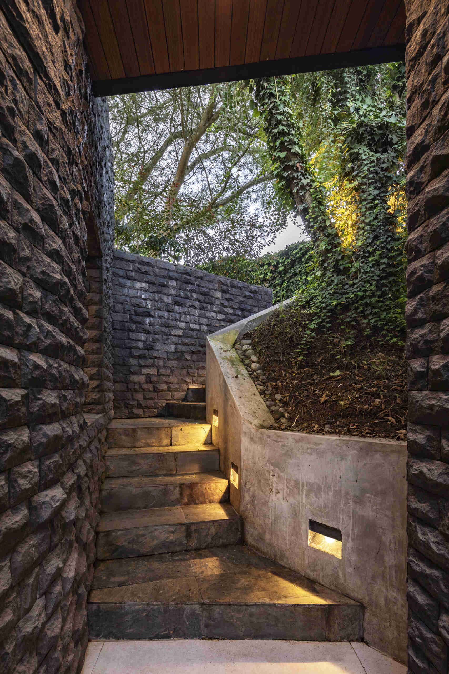 A modern house with stone walls has a staircase winding through the landscape.