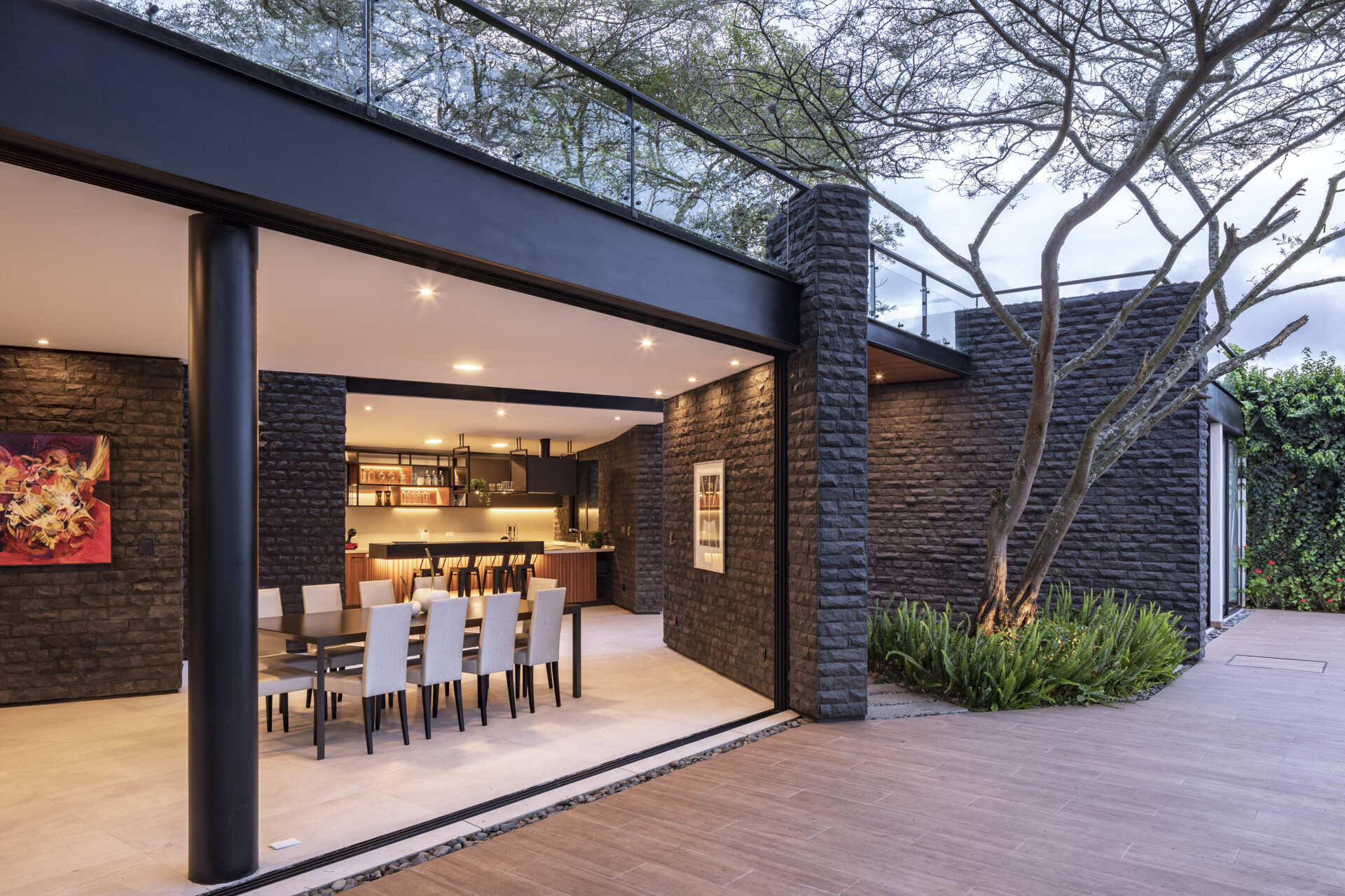 Explore the dining area of the Hidden Stone House, featuring a large dining table, light chairs, dark stone walls and views of the Ecuadorian landscape.