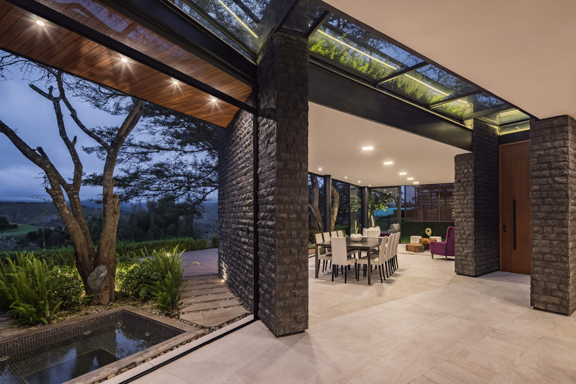 Explore the dining area of the Hidden Stone House, featuring a large dining table, light chairs, dark stone walls and views of the Ecuadorian landscape.