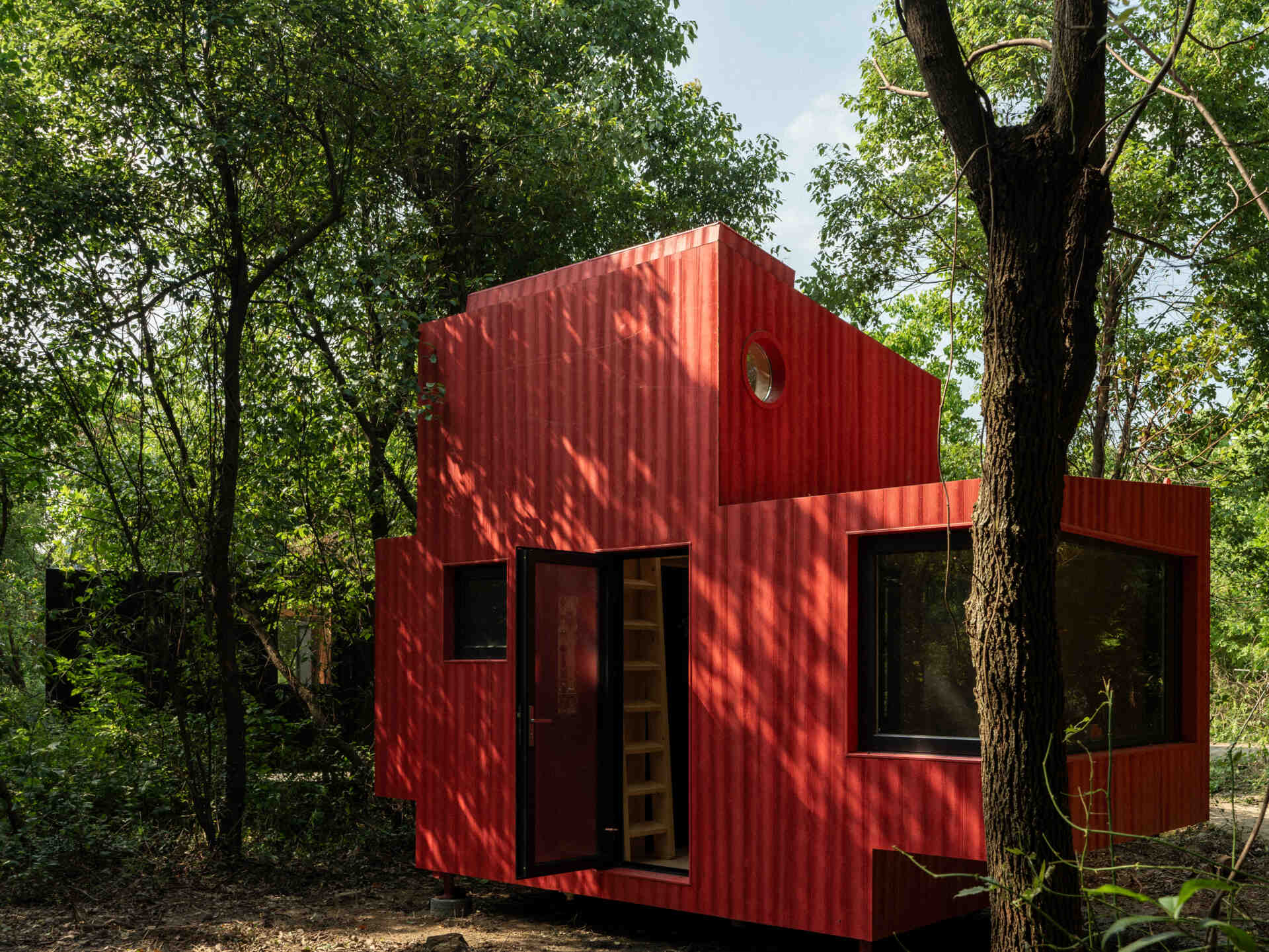 Wiki World’s Red Submarine Cabin brings the playful feeling of a submarine into the forest, with a vibrant red exterior, circular portholes and a compact timber interior.