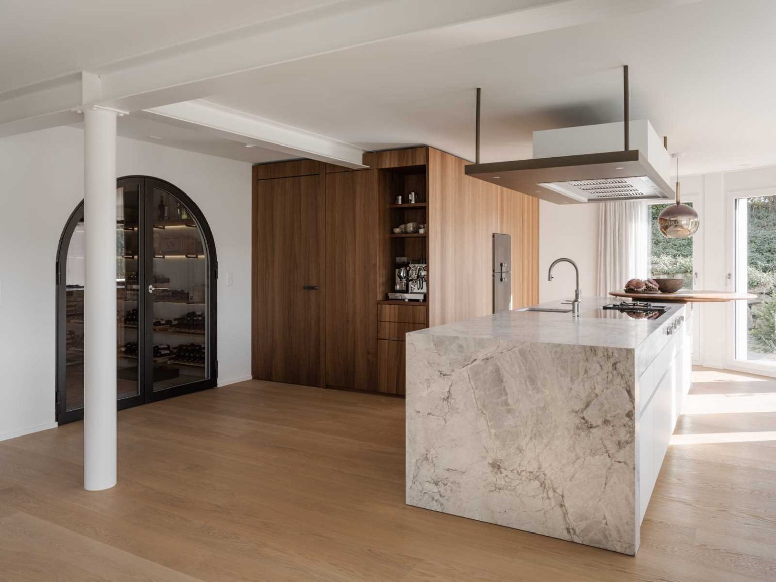 A beautiful Swiss wine cellar sits behind an arched black-framed glass doorway, with wood bottle storage, hidden lighting and a mirror that makes the compact space feel larger.