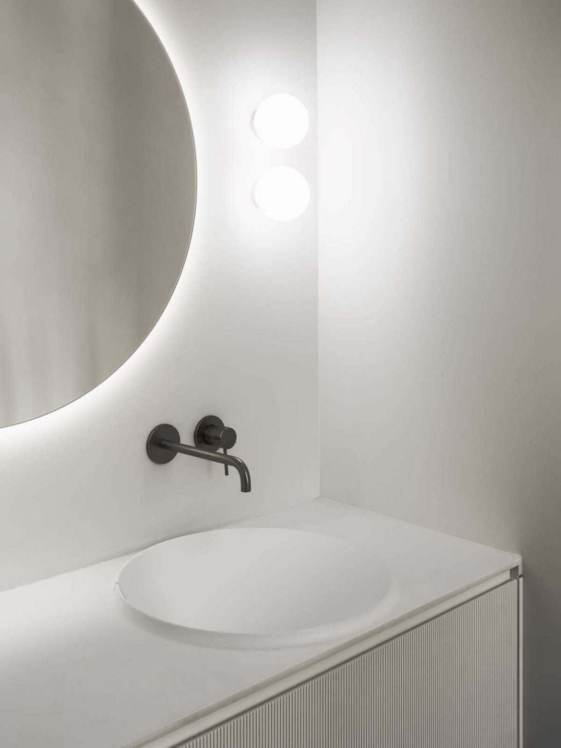 A round backlit mirror, textured white vanity and practical shower niche bring a clean, modern look to the kids' bathroom in this Swiss home.