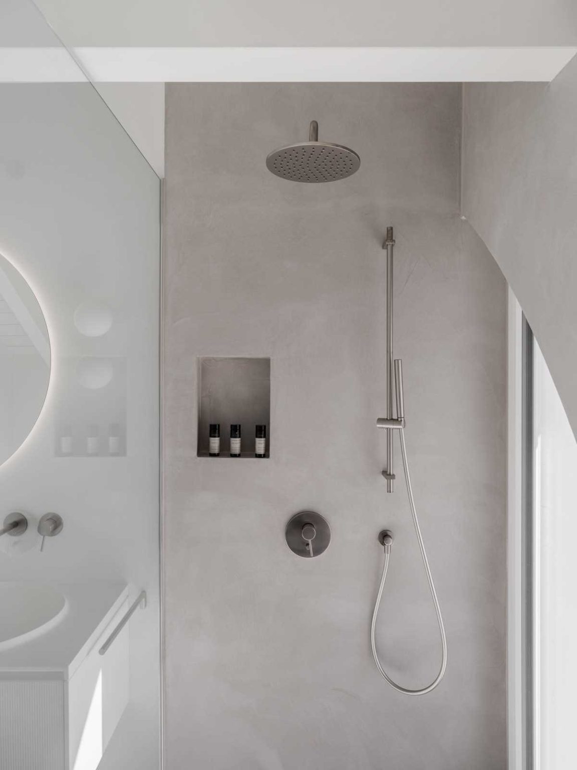 A round backlit mirror, textured white vanity and practical shower niche bring a clean, modern look to the kids' bathroom in this Swiss home.