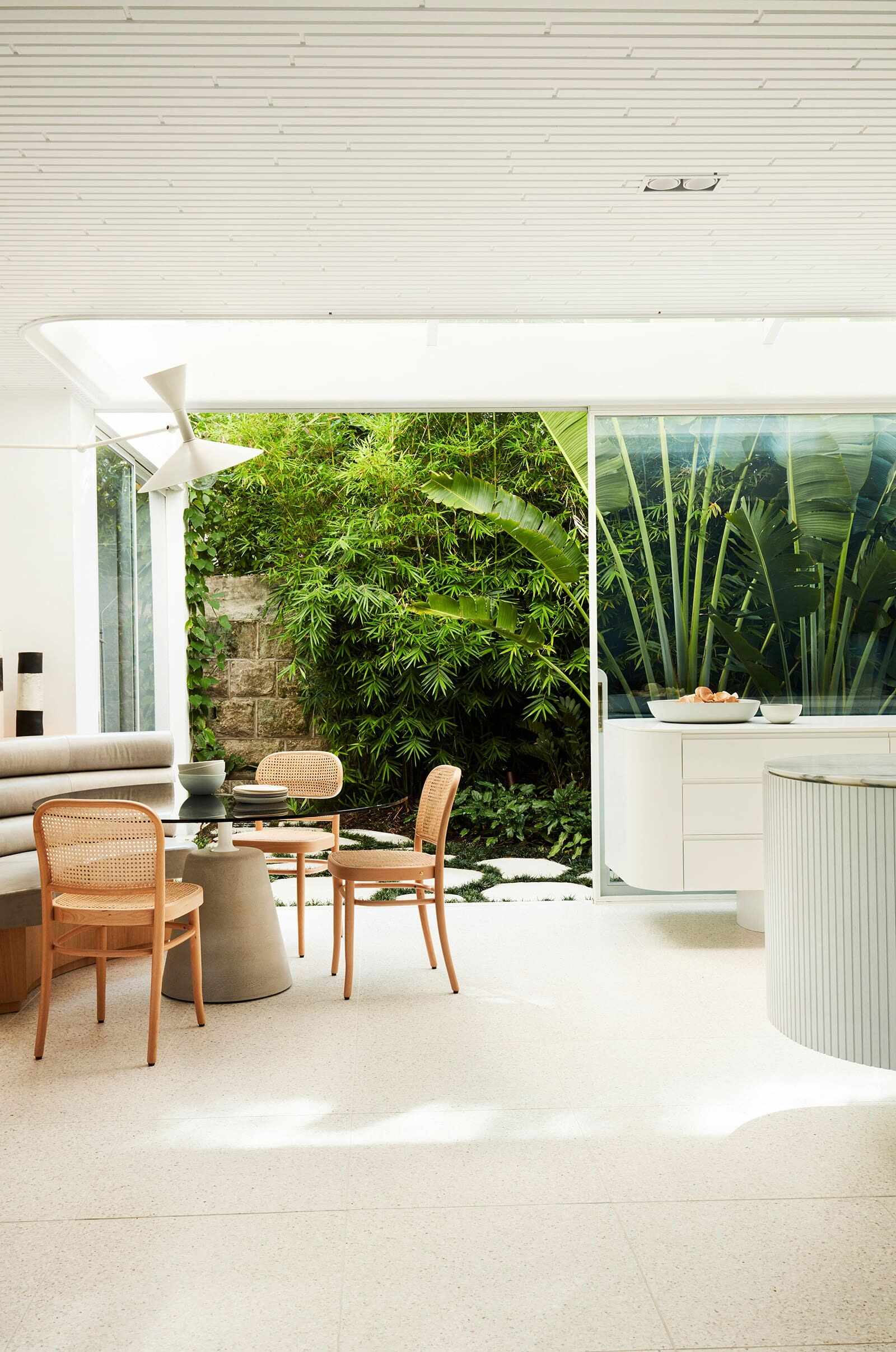 A light-filled open-plan kitchen, breakfast table and dining area sit beneath curved ceilings, with expansive glass opening the home toward its lush garden.