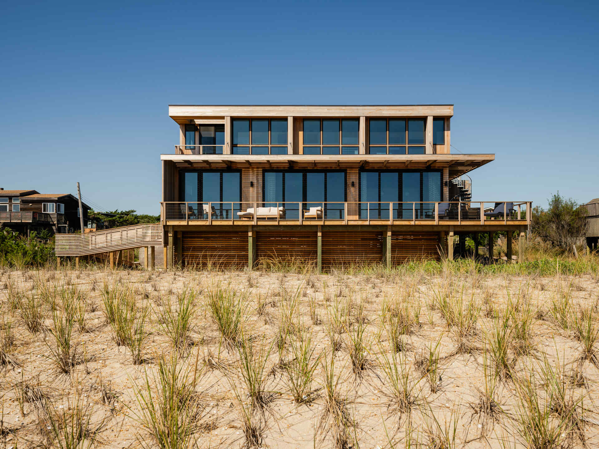 Explore the cedar-clad architecture of Surf Road House by Coughlin Scheel Architects in Ocean Beach, Fire Island. Elevated on timber pilings, this coastal home combines ocean-facing windows, layered facades, and a shaded wood trellis.