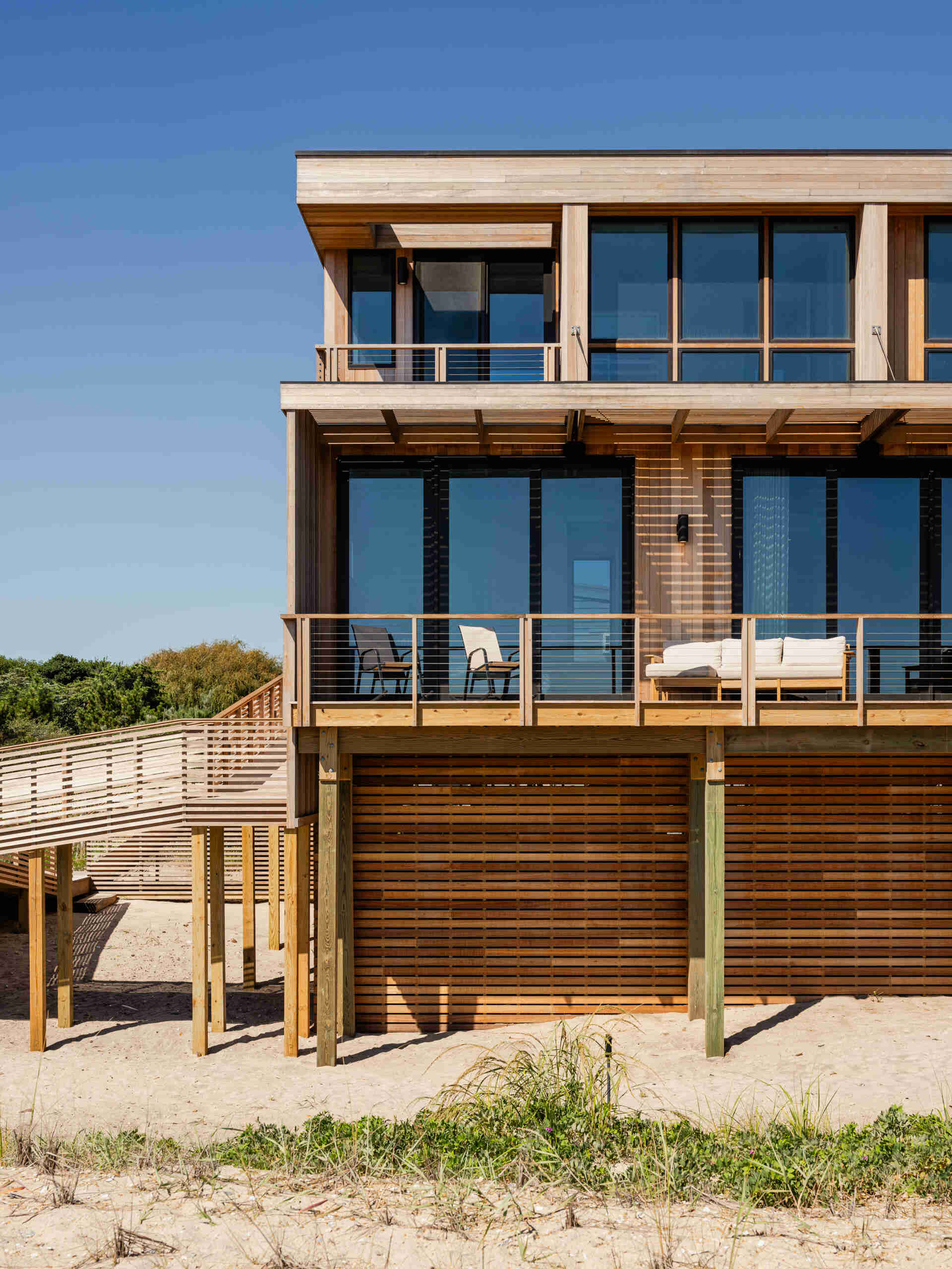 Explore the cedar-clad architecture of Surf Road House by Coughlin Scheel Architects in Ocean Beach, Fire Island. Elevated on timber pilings, this coastal home combines ocean-facing windows, layered facades, and a shaded wood trellis.
