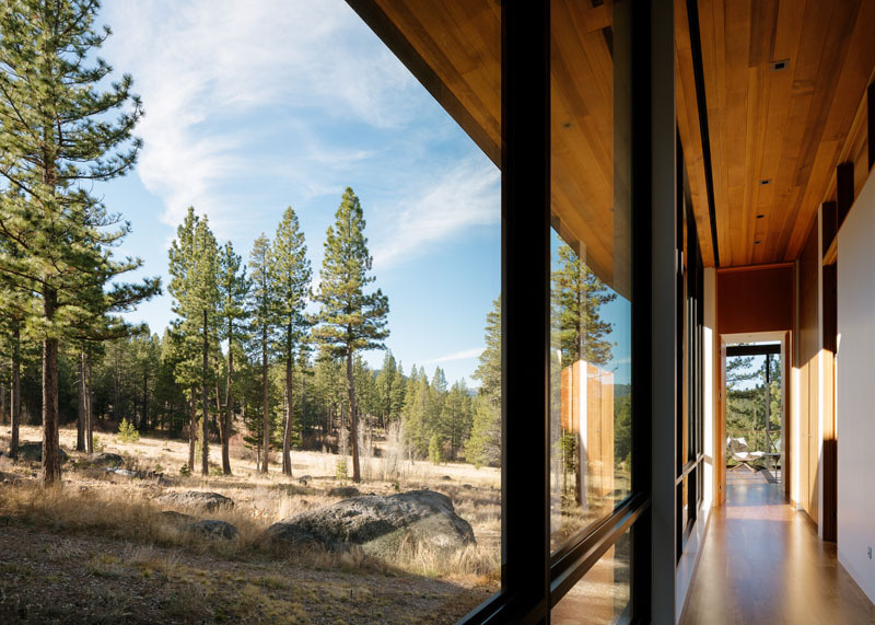 Follow the glass-lined hallway to the master bedroom, where black-framed windows, white interiors and a wood ceiling frame views of the landscape.