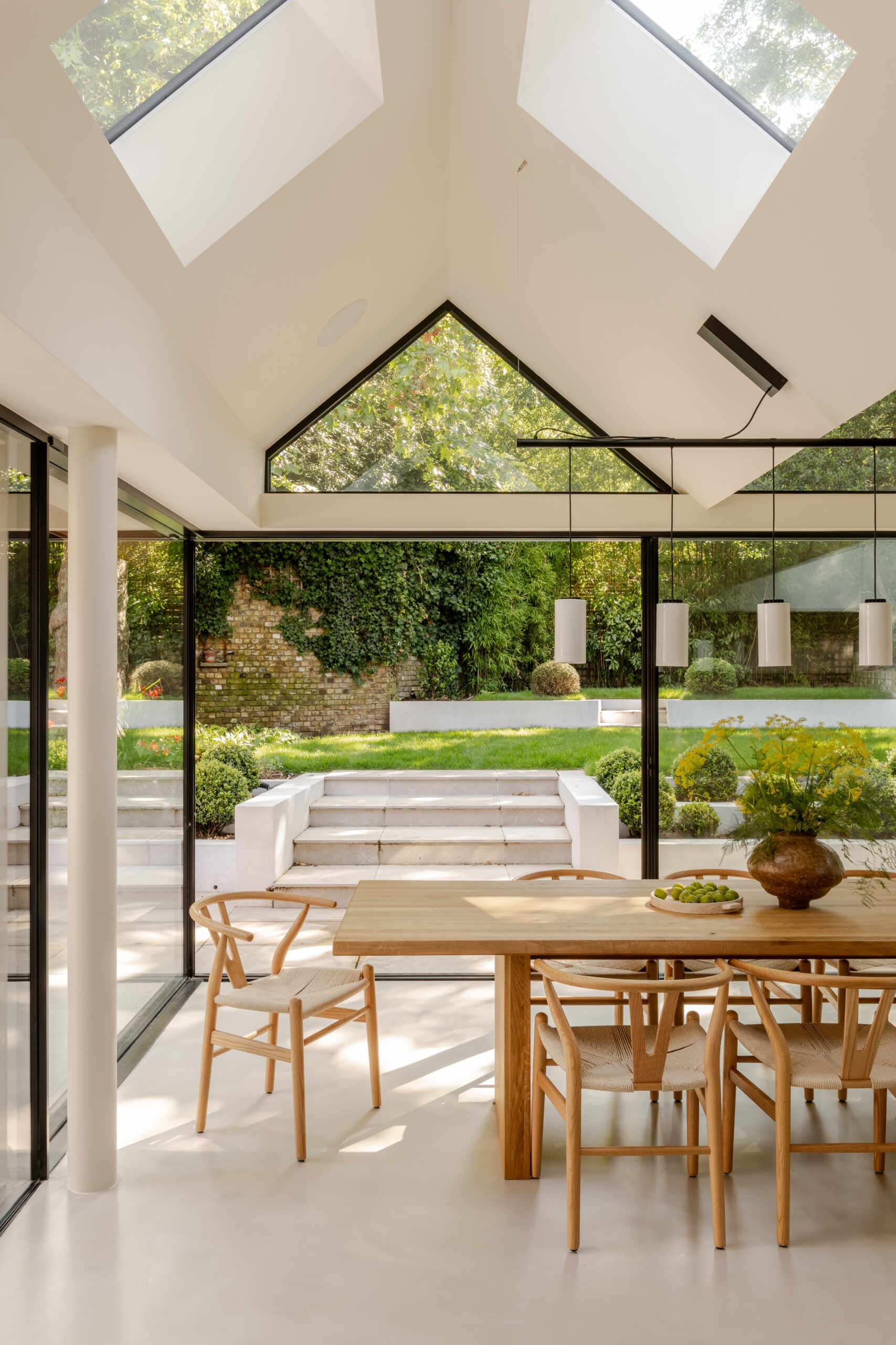 Explore the light-filled dining area at Thirsk Cottage, featuring black-framed glazing, warm wood, woven chairs and views towards the garden.