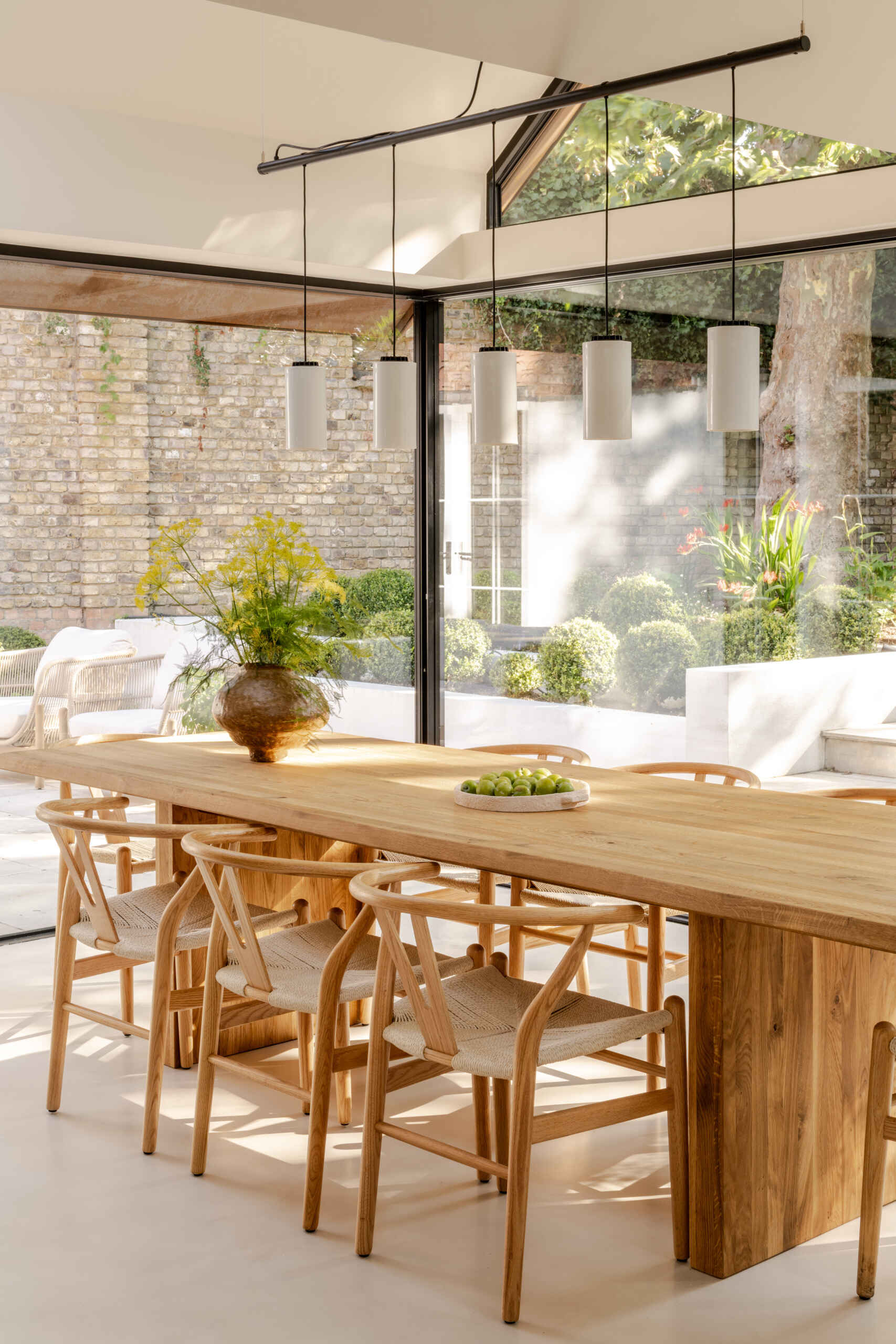 Explore the light-filled dining area at Thirsk Cottage, featuring black-framed glazing, warm wood, woven chairs and views towards the garden.