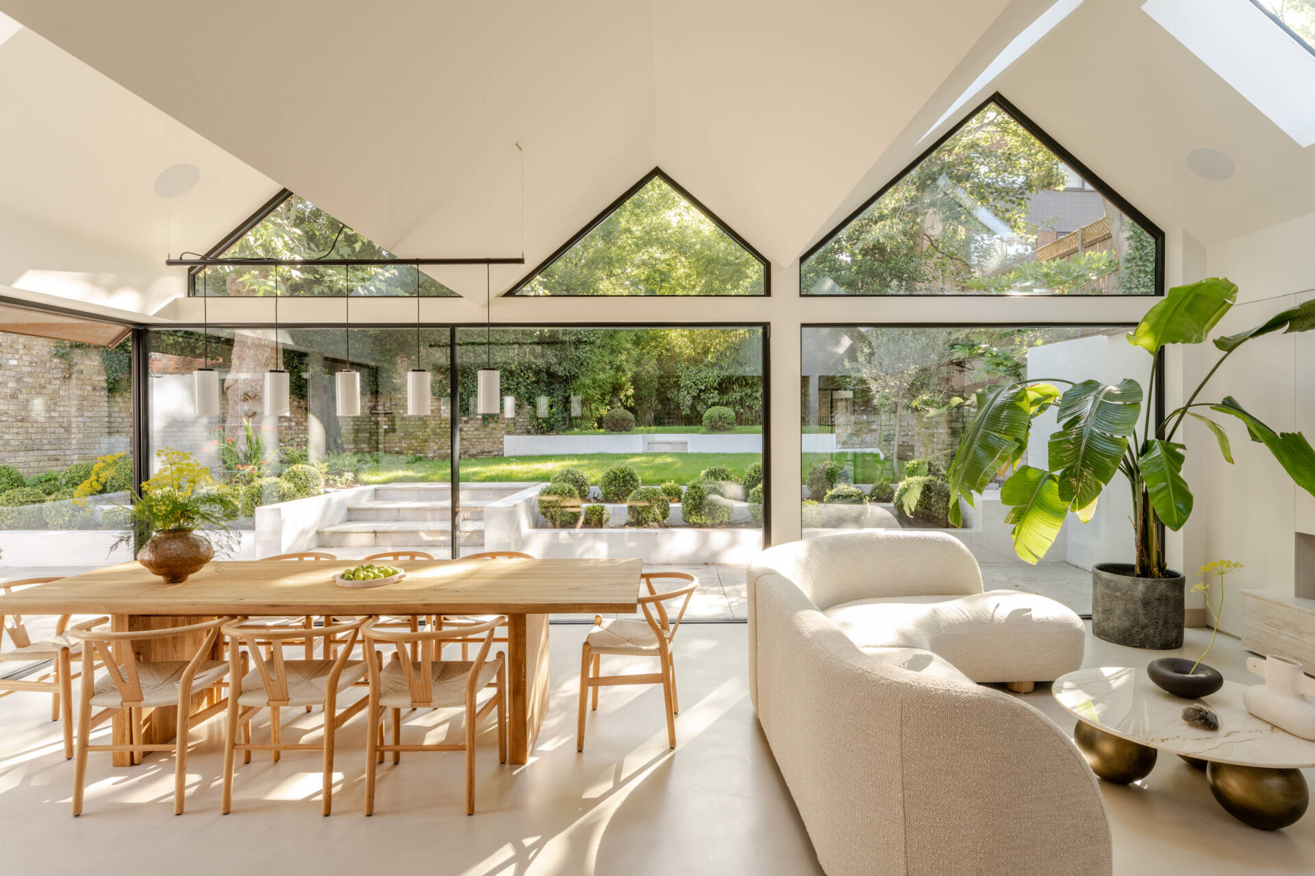 Explore the light-filled dining area at Thirsk Cottage, featuring black-framed glazing, warm wood, woven chairs and views towards the garden.
