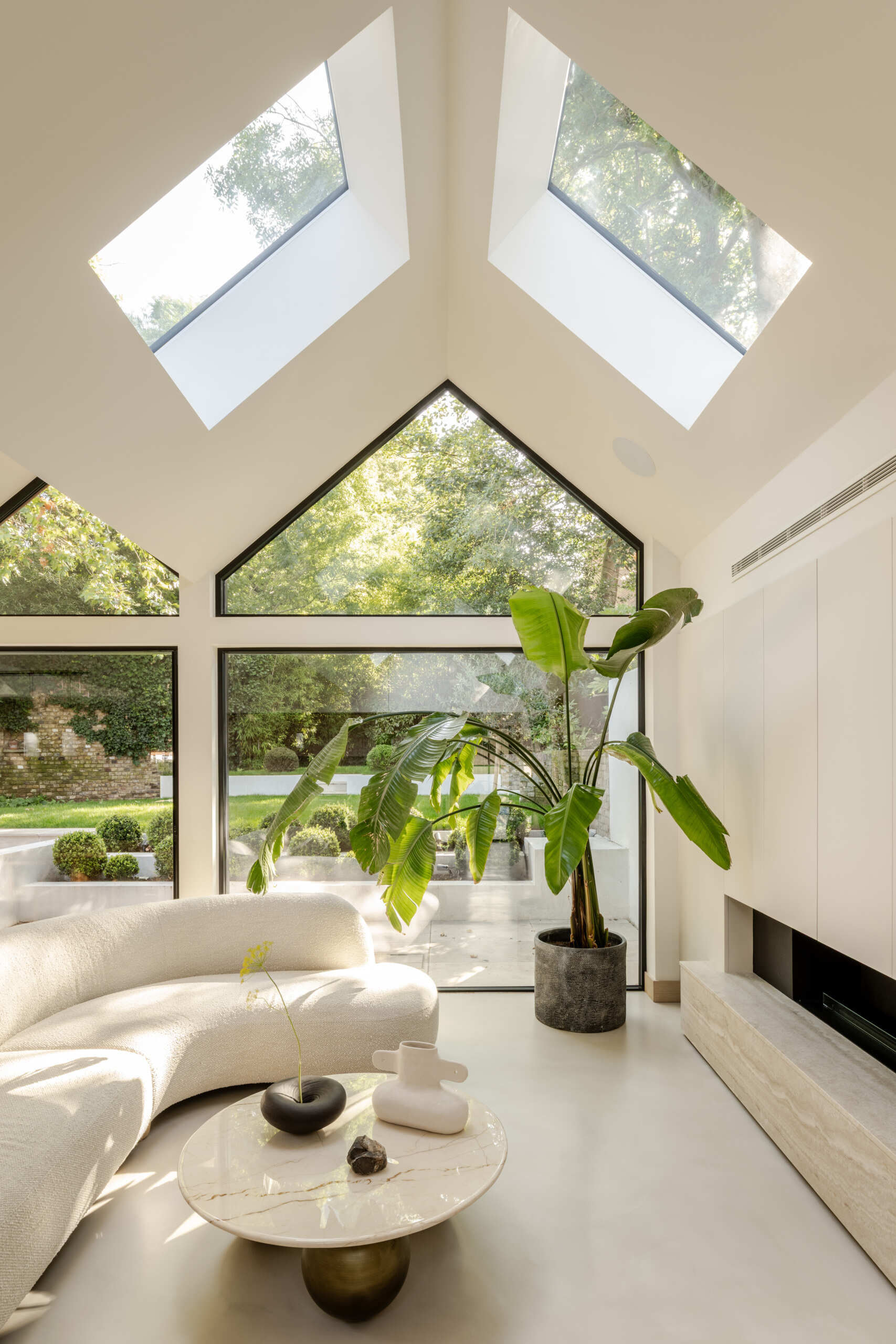 Step inside the living room at Thirsk Cottage, where a vaulted ceiling, black-framed windows, skylights and a long fireplace create a bright and comfortable space.