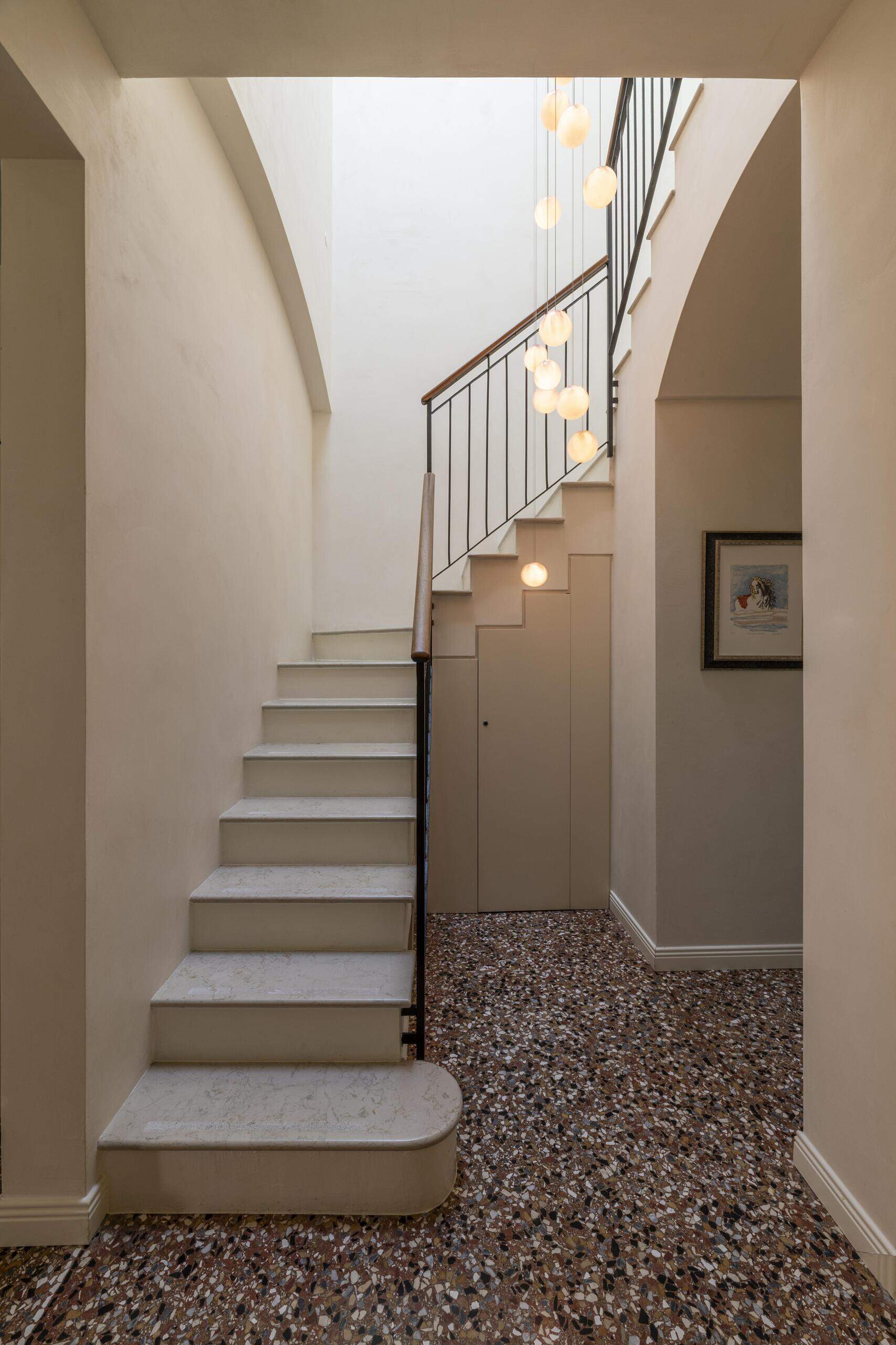 A historic Italian apartment corridor reveals its structural tie rods after the suspended ceiling was removed, paired with a parchment cabinet and sculptural brass handles.