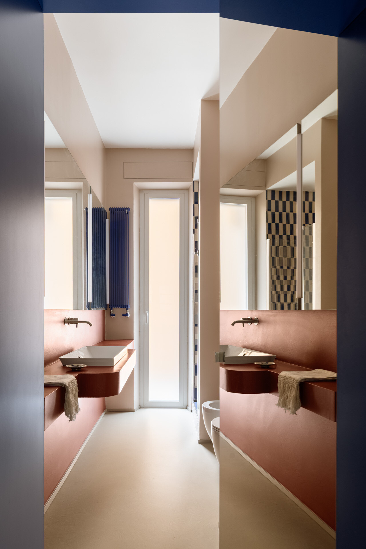 A colorful contemporary bathroom features a floating vanity, white vessel sink, large illuminated mirrors, cobalt-blue radiator, and a walk-in shower with graphic blue-and-white rectangular tiles.