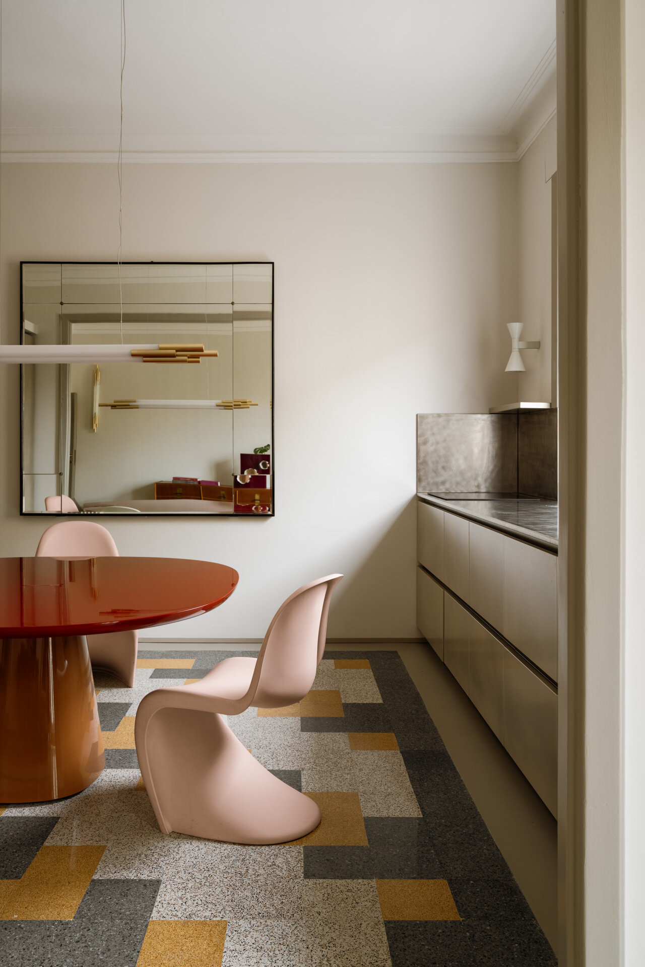 This contemporary kitchen and dining room in Rome features a glossy two-tone B&B Italia dining table, pale pink Vitra Panton Chairs, a gold-lacquered Arrital kitchen, brushed-steel countertops, and restored geometric graniglia flooring.