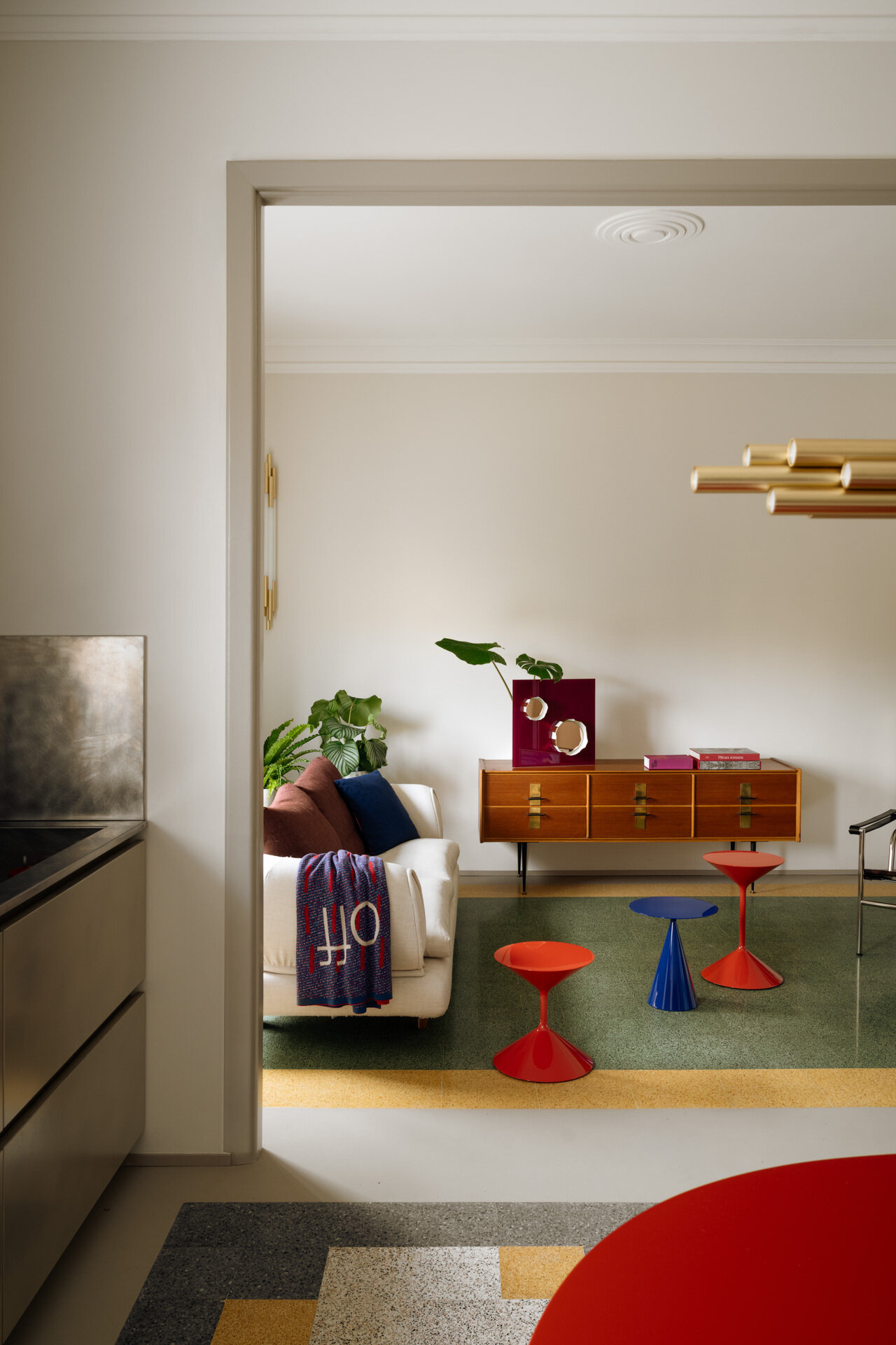 A colorful living room in a renovated 1930s Rome apartment features original green and yellow graniglia flooring, a white Dema sofa, sculptural Zanotta coffee tables, an LC1 armchair by Cassina, and vintage furniture.