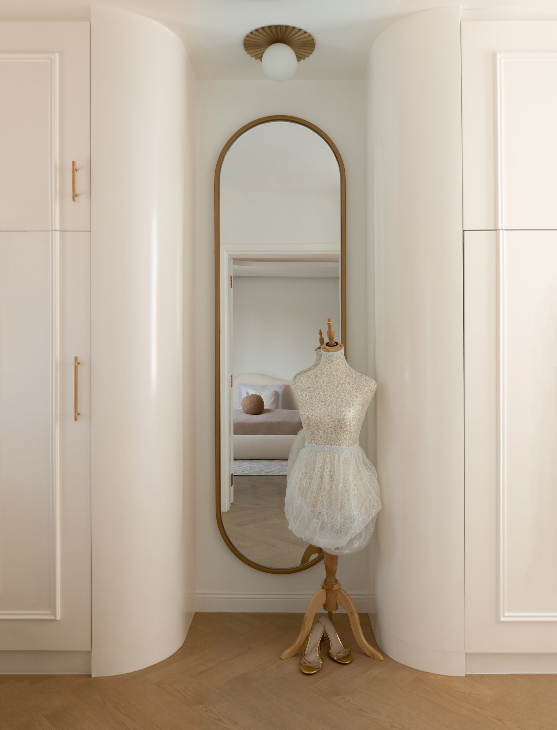A contemporary bedroom inside The White Arcade in Dubai. Designed by D’Ora Tokai Designs, this youthful bedroom features a custom curved upholstered bed, pastel lavender bedside tables, colourful wall art, a textured white rug, and an adjoining dressing area.