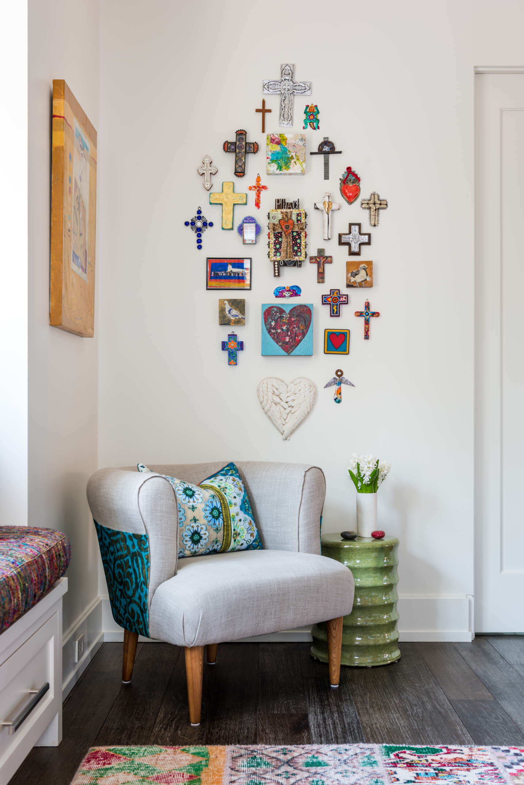 A colorful bedroom with vibrant patterned accent wall, a turquoise upholstered bed, oversized beaded chandelier, multicolored patchwork rug, yellow dresser, and built-in window seat with storage.