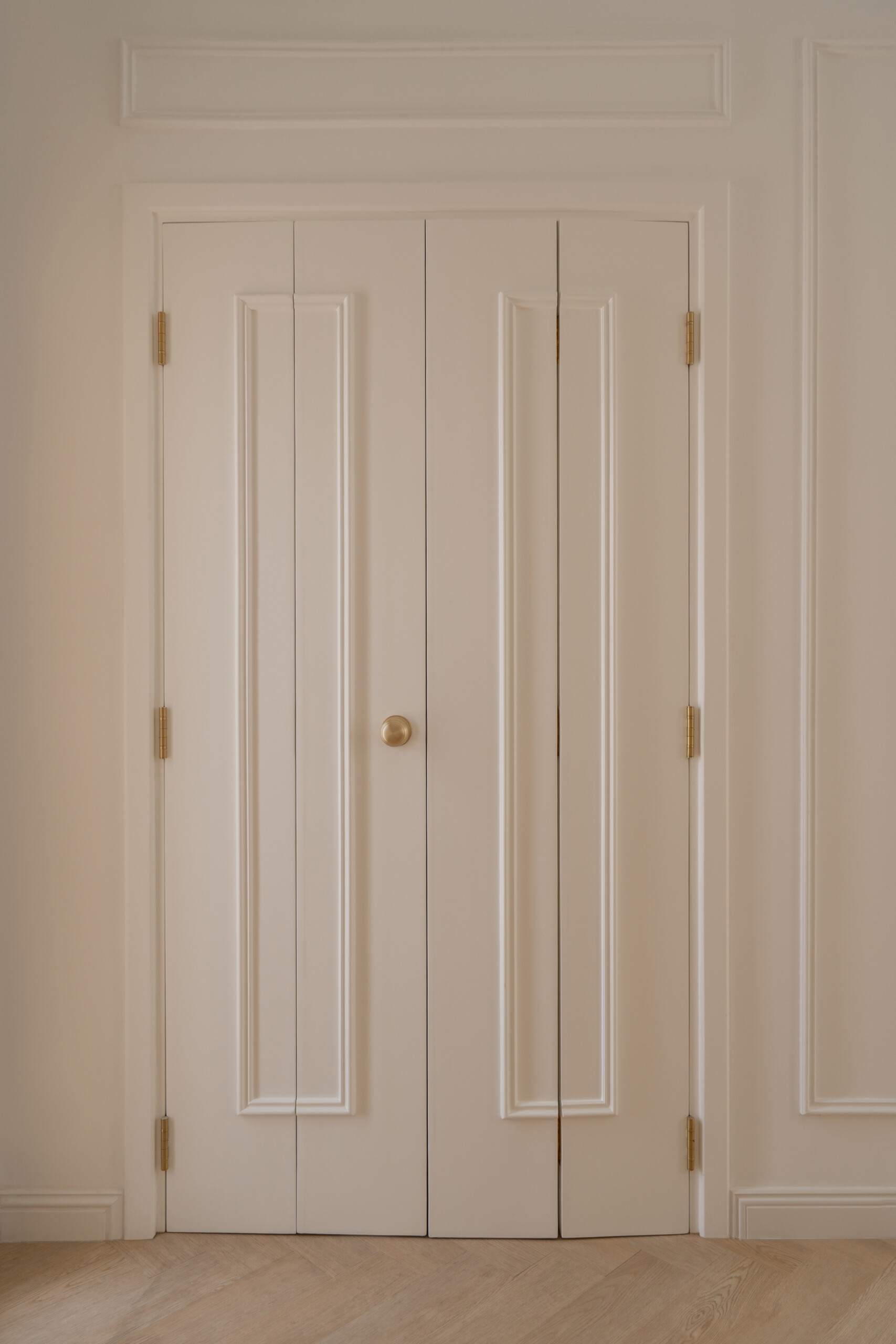 Hidden behind elegant bifold doors, this coat room at The White Arcade in Dubai features oak-lined walls, built-in bench seating, concealed drawers, brass hooks, and practical shelving. A stylish small-space storage idea by D’Ora Tokai Designs.