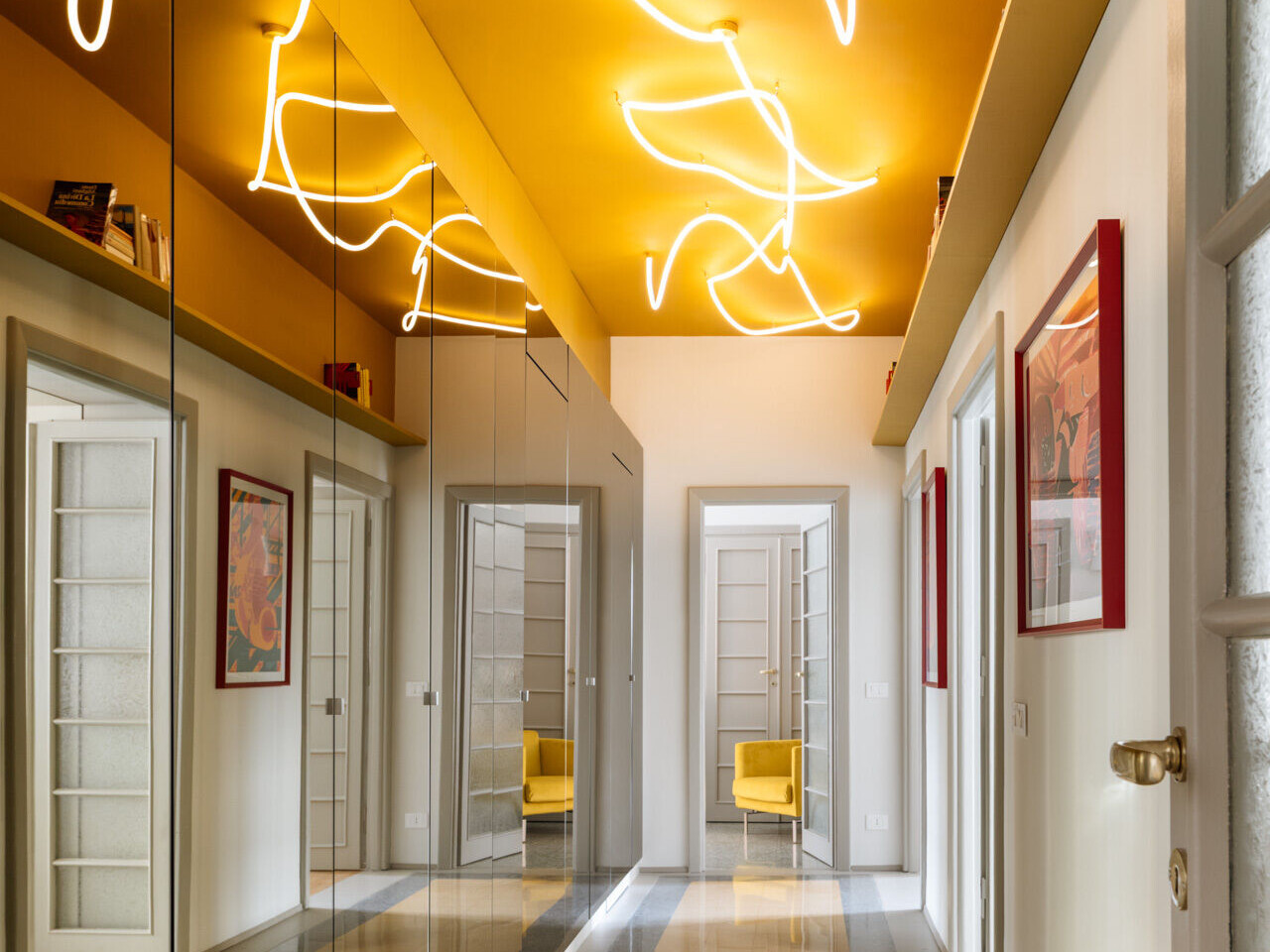 A unique apartment hallway in Rome features a vivid yellow ceiling with custom white LED neon lighting inspired by Lucio Fontana. Designed by Neeo Design as part of a renovation by Raffaella Falbo, the abstract light installation is reflected in a mirrored wall.