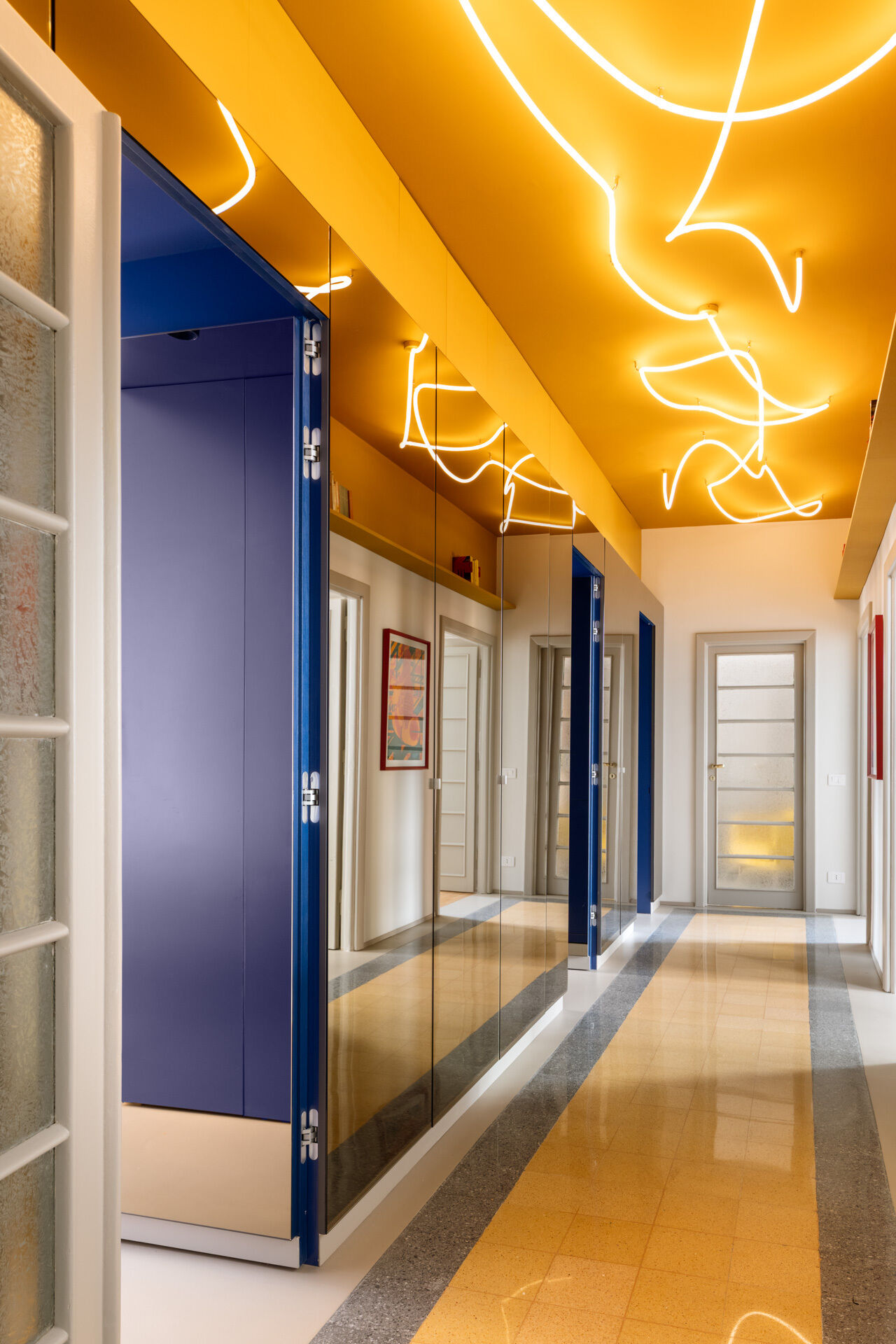 A unique apartment hallway in Rome features a vivid yellow ceiling with custom white LED neon lighting inspired by Lucio Fontana. Designed by Neeo Design as part of a renovation by Raffaella Falbo, the abstract light installation is reflected in a mirrored wall.