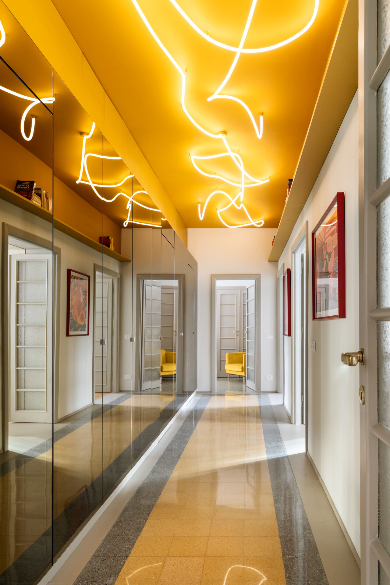 A unique apartment hallway in Rome features a vivid yellow ceiling with custom white LED neon lighting inspired by Lucio Fontana. Designed by Neeo Design as part of a renovation by Raffaella Falbo, the abstract light installation is reflected in a mirrored wall.