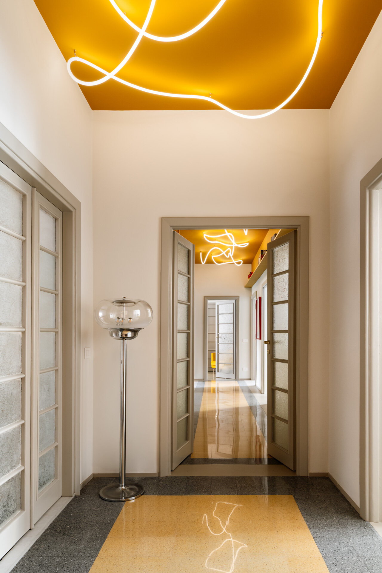 A unique apartment hallway in Rome features a vivid yellow ceiling with custom white LED neon lighting inspired by Lucio Fontana. Designed by Neeo Design as part of a renovation by Raffaella Falbo, the abstract light installation is reflected in a mirrored wall.