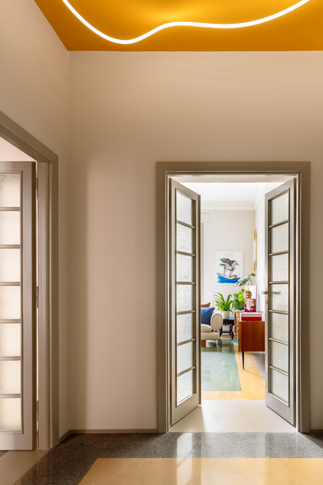 A unique apartment hallway in Rome features a vivid yellow ceiling with custom white LED neon lighting inspired by Lucio Fontana. Designed by Neeo Design as part of a renovation by Raffaella Falbo, the abstract light installation is reflected in a mirrored wall.