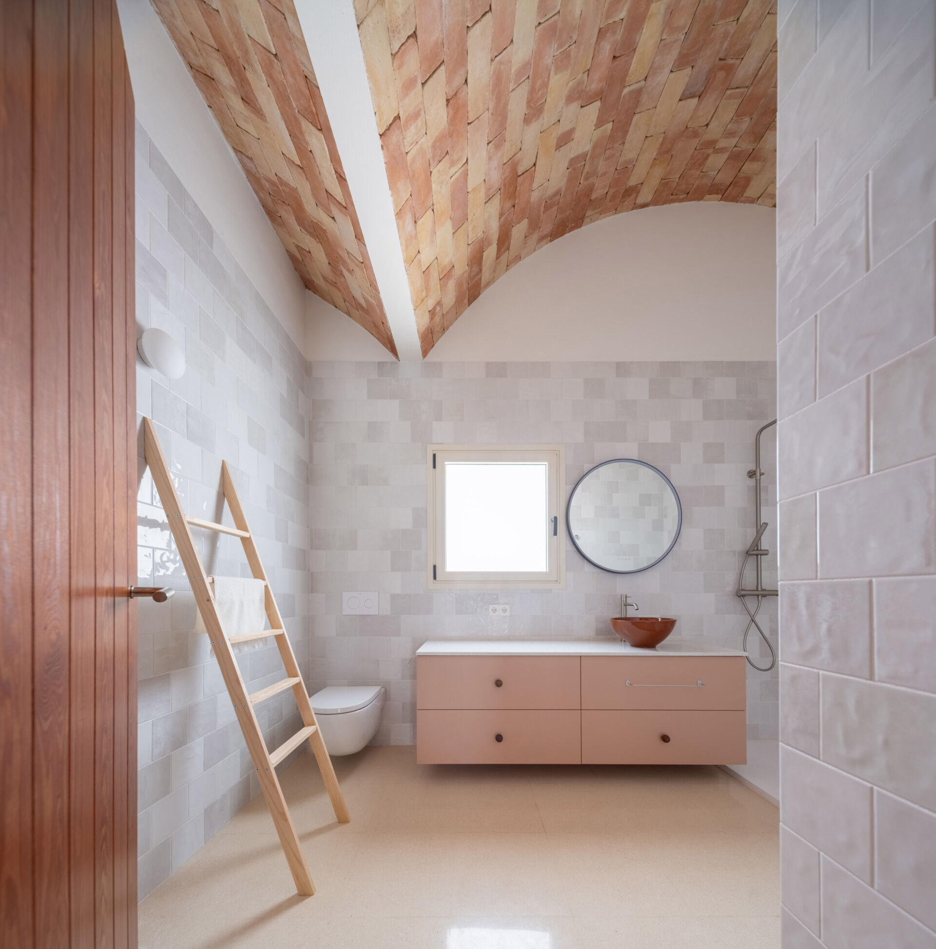 Discover the bathrooms at Casa Vereda in Spain, featuring soft pink floating vanities, terracotta vessel sinks, pale grey wall tiles, and exposed brick vaulted ceilings.
