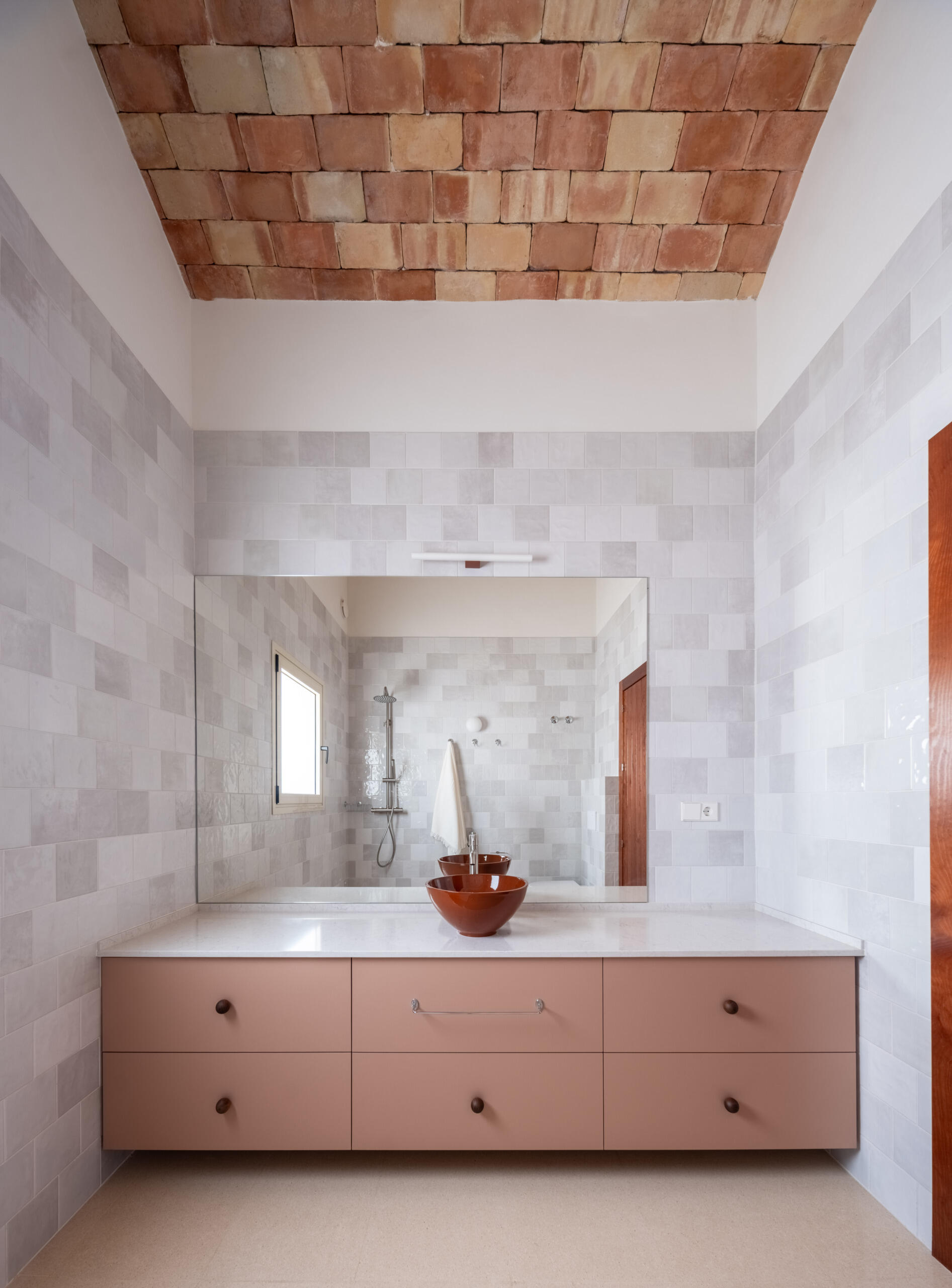 Discover the bathrooms at Casa Vereda in Spain, featuring soft pink floating vanities, terracotta vessel sinks, pale grey wall tiles, and exposed brick vaulted ceilings.