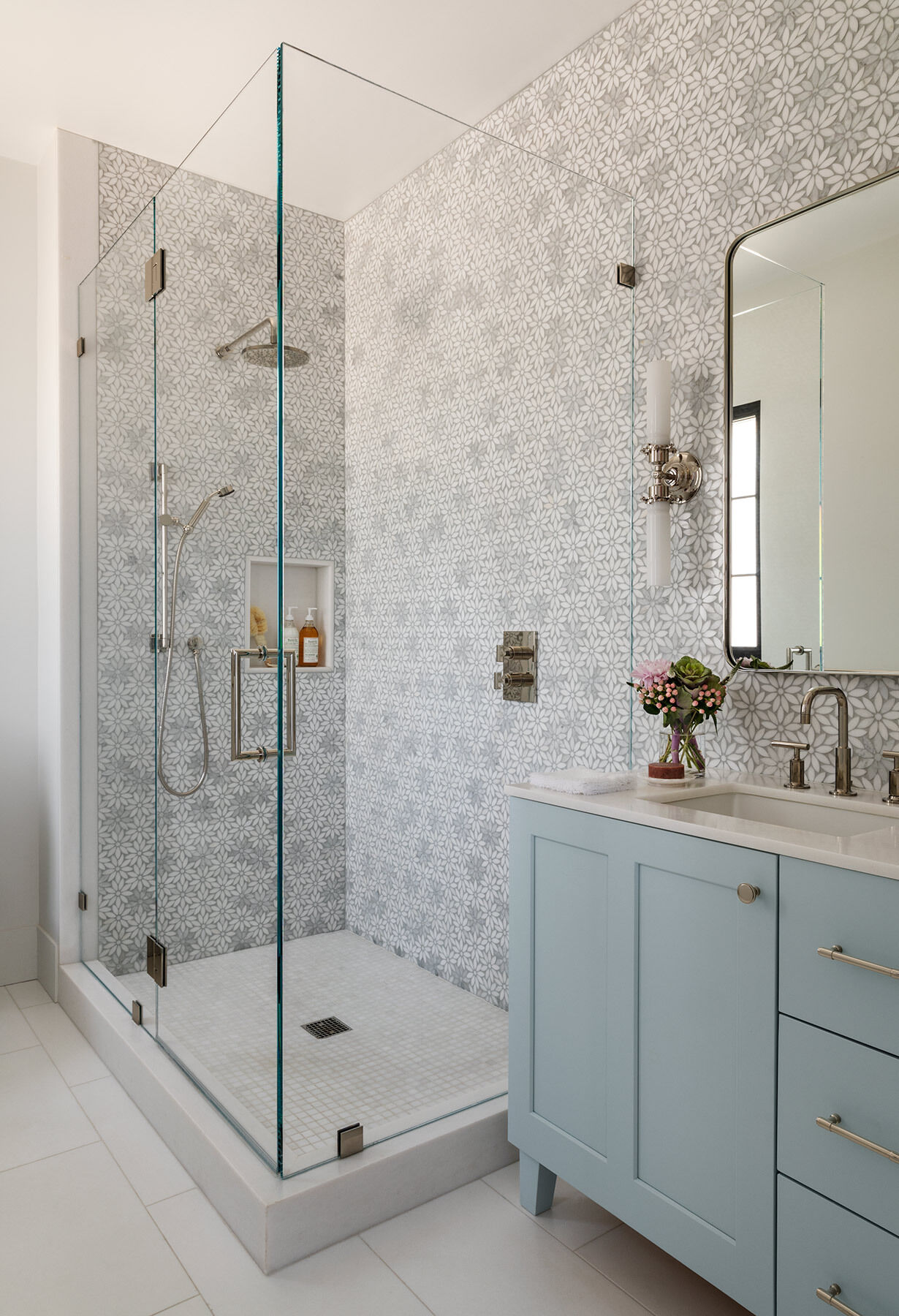 A second bathroom in the Atherton Residence pairs floral mosaic shower walls with a frameless glass enclosure, polished metal fittings and a pale blue vanity for a softer, more decorative take on modern bathroom design.