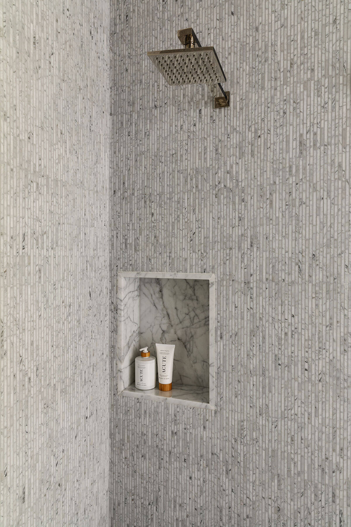 This compact bathroom in the Atherton Residence pairs grey mosaic shower walls, dark stone flooring, frameless glass, a marble-lined niche and light timber cabinetry for a clean, modern finish.