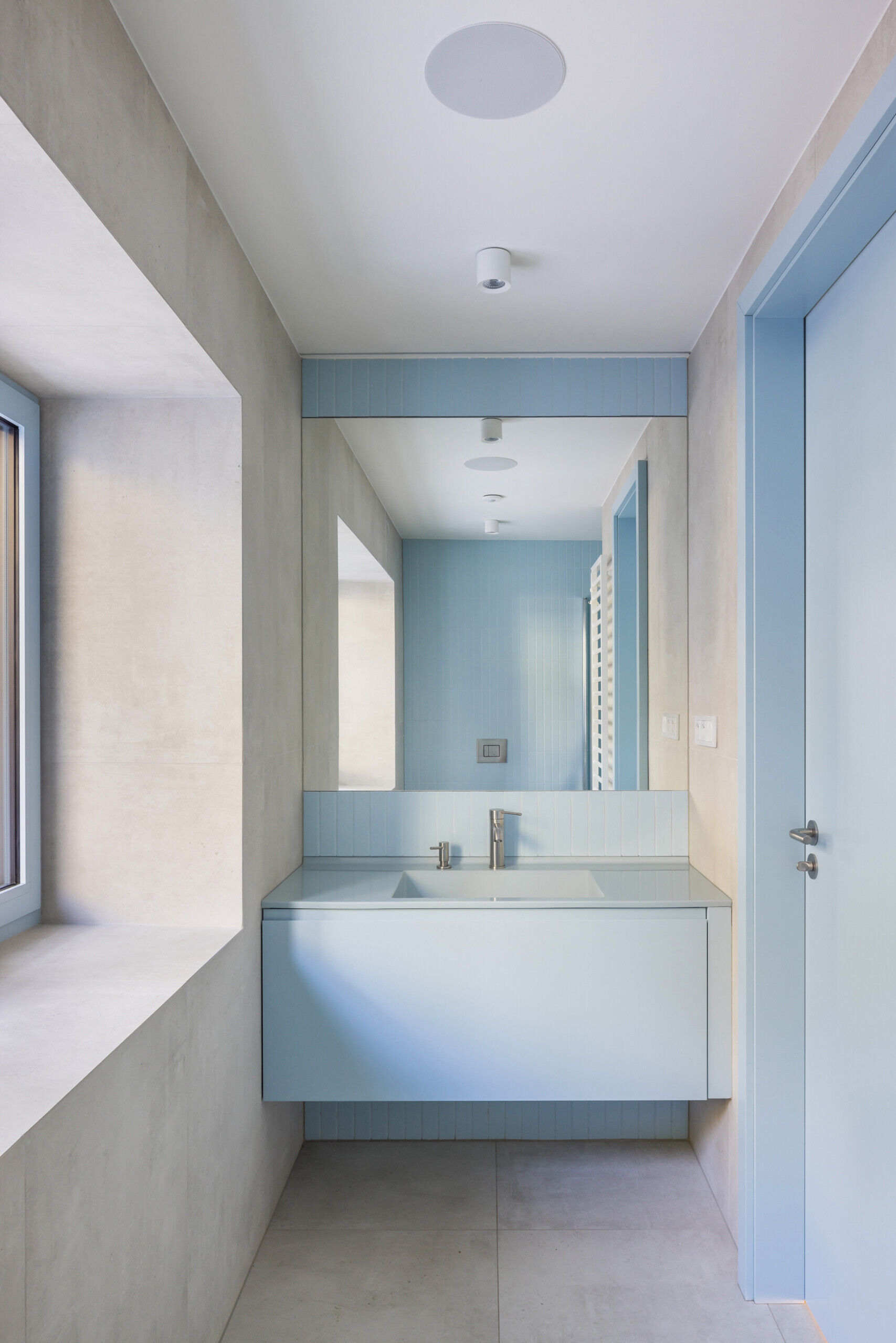 Discover the colorful bathrooms and smaller interior spaces of this renovated Prague home. Red and pale blue bathroom cabinetry, a lavender upholstered window bench, circular wall lights, and refined architectural details bring personality to the contemporary design.