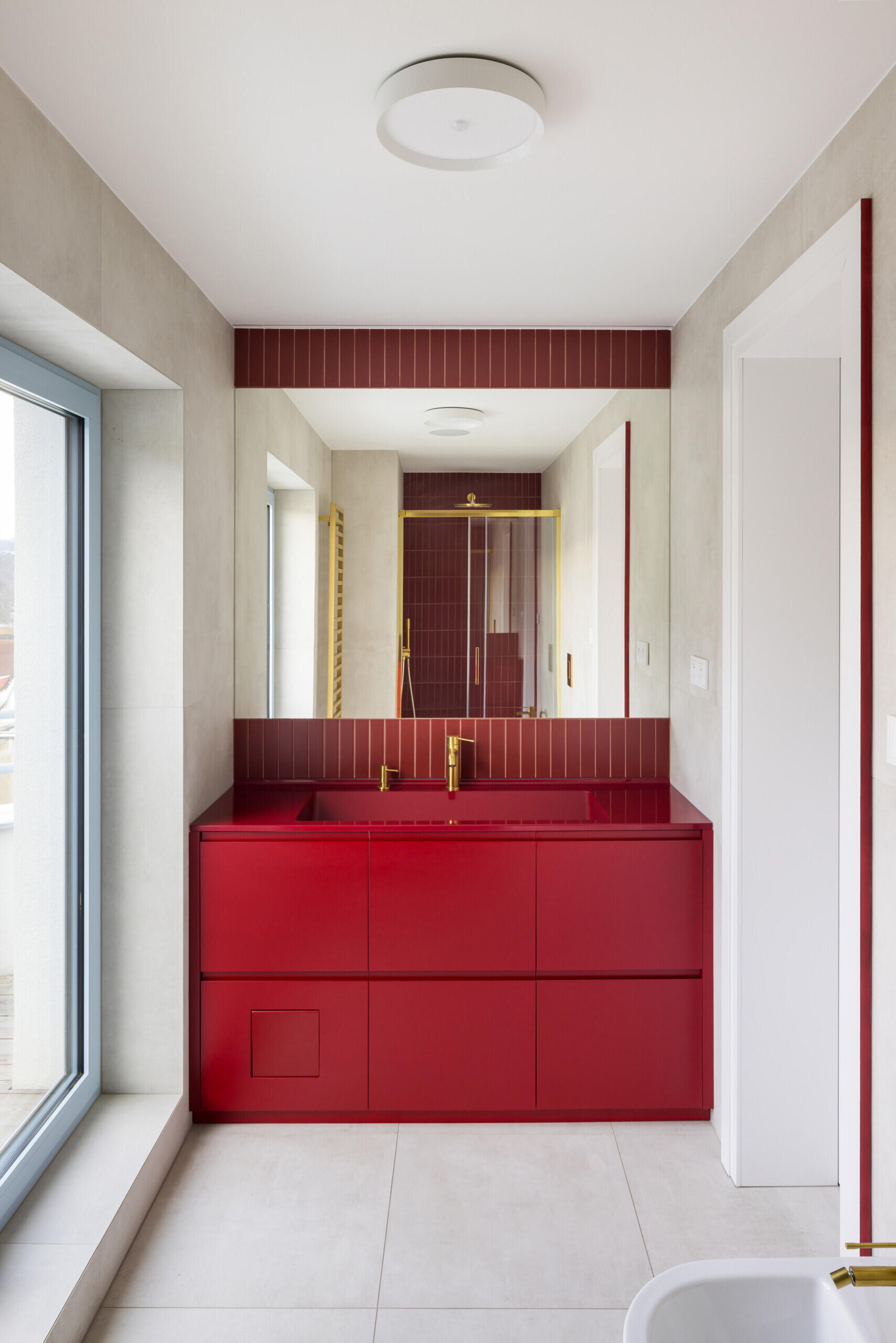 Discover the colorful bathrooms and smaller interior spaces of this renovated Prague home. Red and pale blue bathroom cabinetry, a lavender upholstered window bench, circular wall lights, and refined architectural details bring personality to the contemporary design.