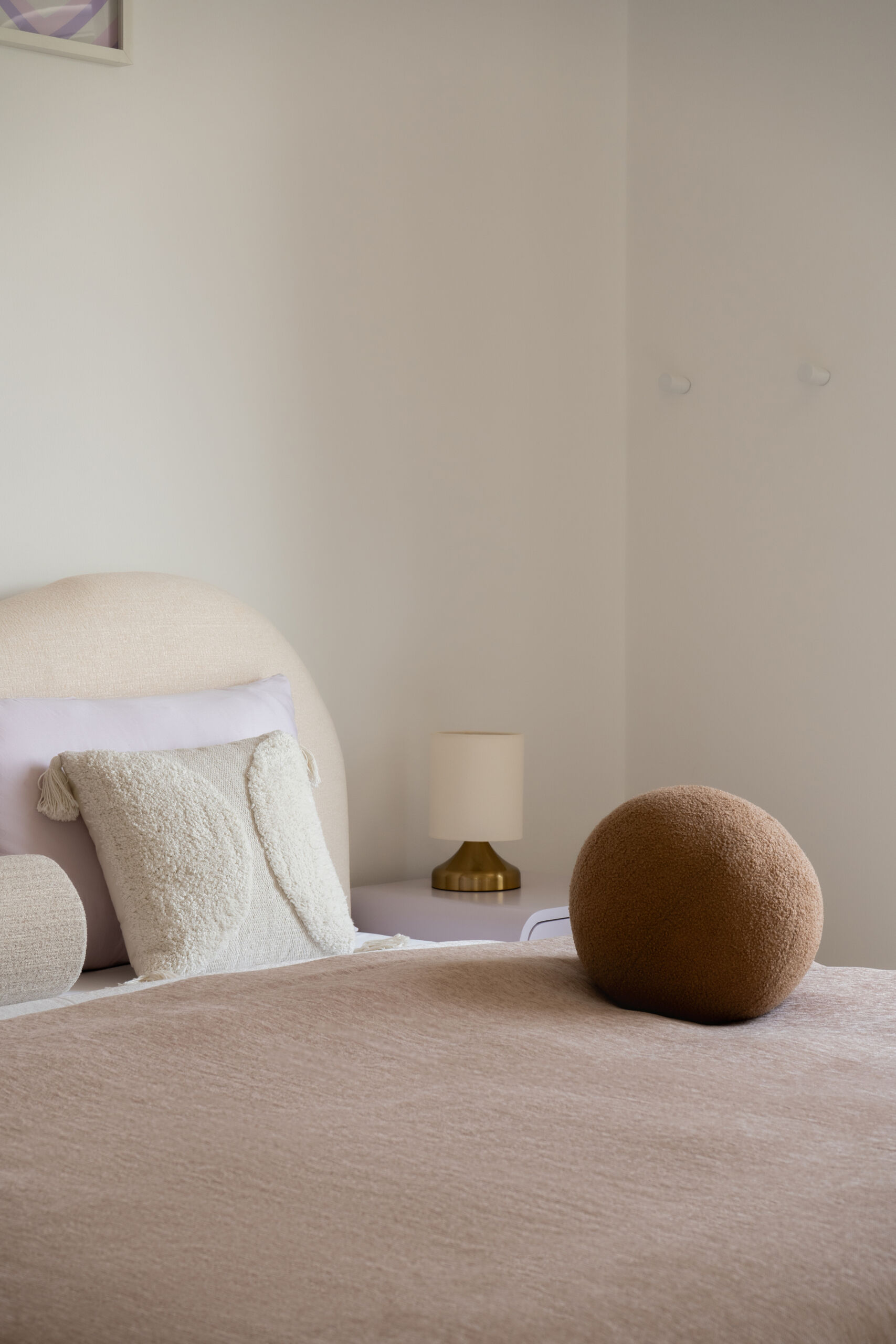 A contemporary bedroom inside The White Arcade in Dubai. Designed by D’Ora Tokai Designs, this youthful bedroom features a custom curved upholstered bed, pastel lavender bedside tables, colourful wall art, a textured white rug, and an adjoining dressing area.