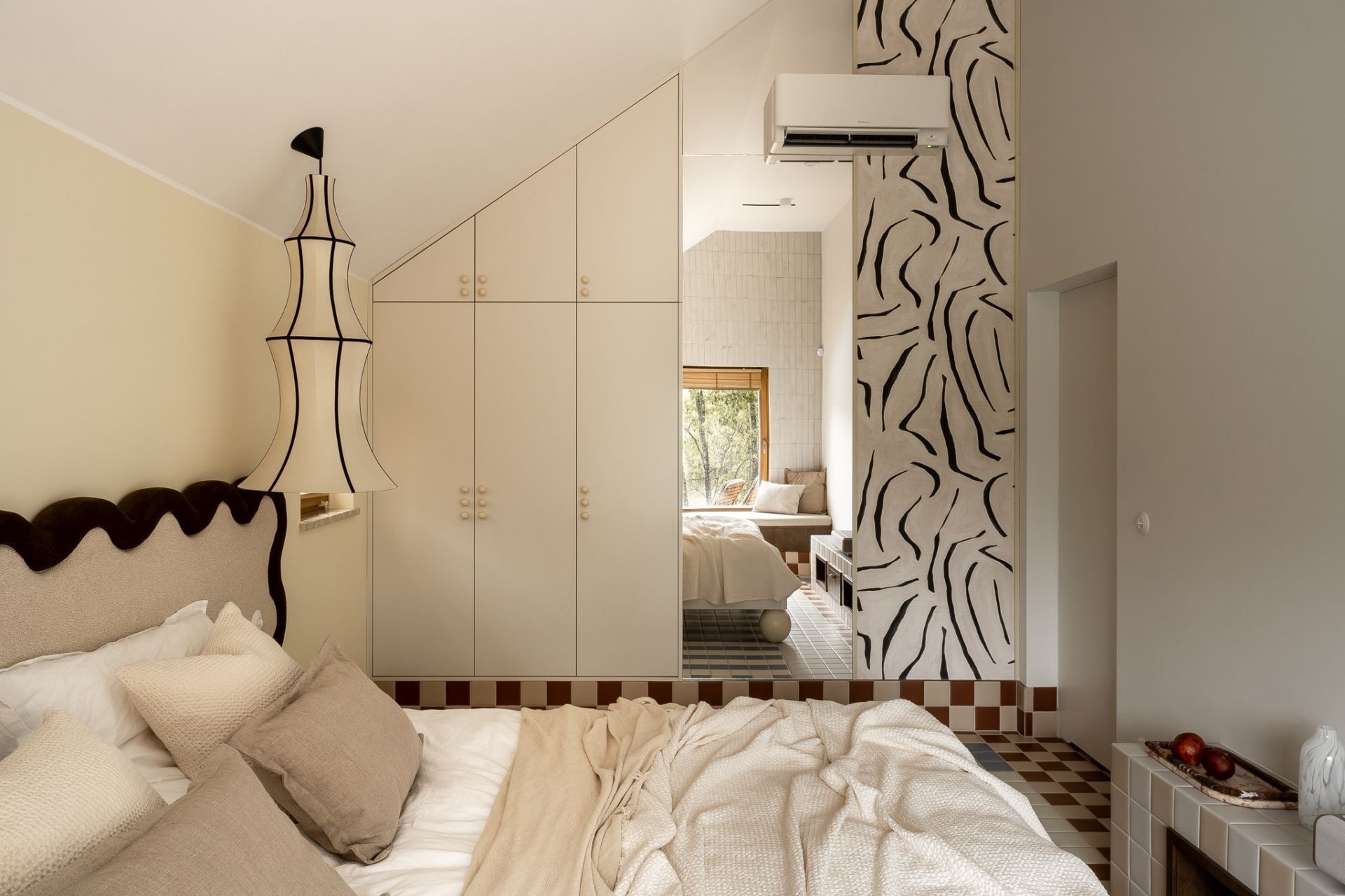 Bedroom design inspiration featuring a sculptural wave-shaped headboard, neutral bedding, unusual pendant lighting, custom fitted wardrobes, and bold black-and-white wallpaper.