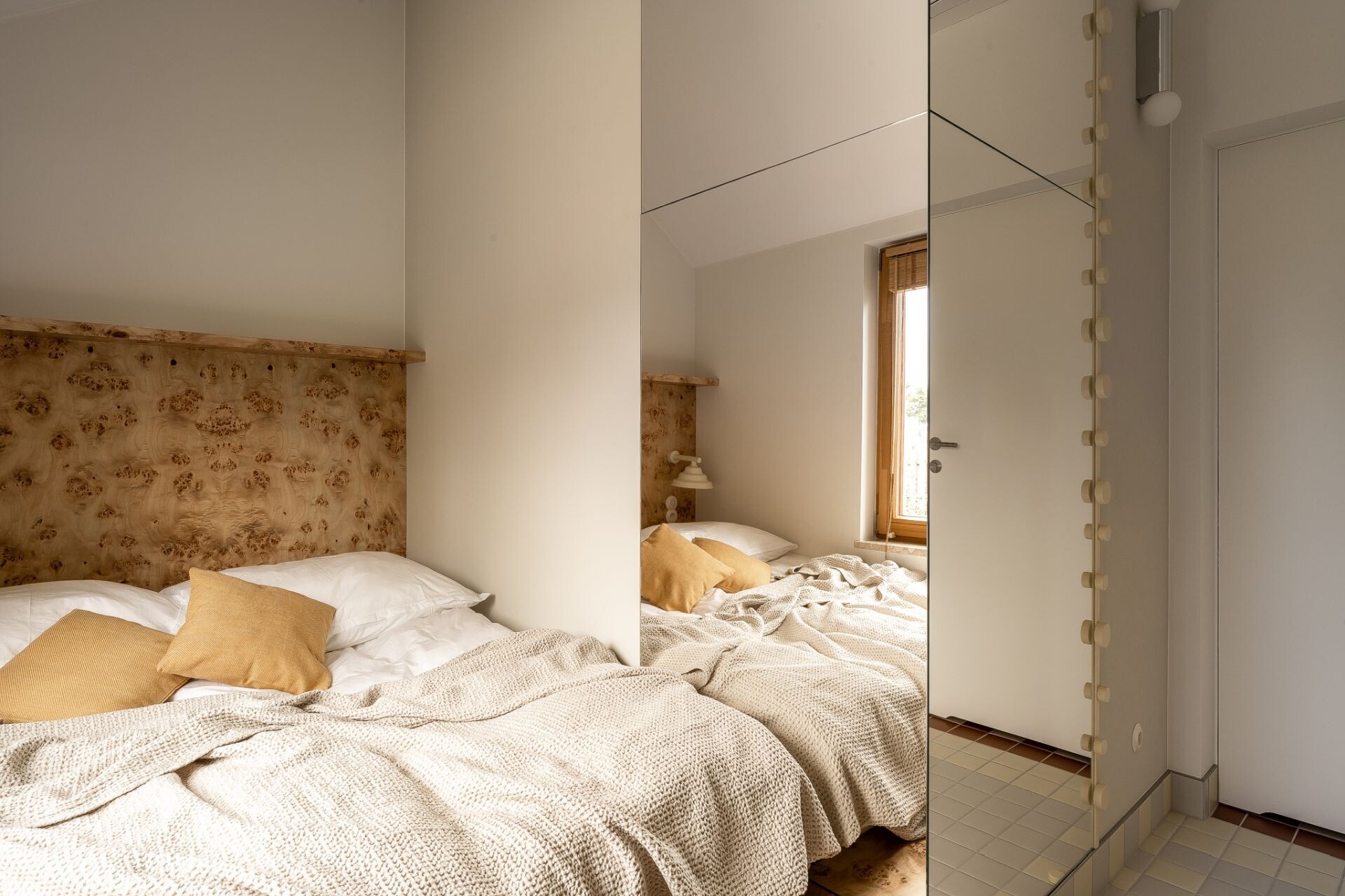 Contemporary bedroom with a poplar burl wood headboard, soft yellow accents, mirrored wall, custom floating dressing table, sculptural yellow chair, and two wavy decorative mirrors.