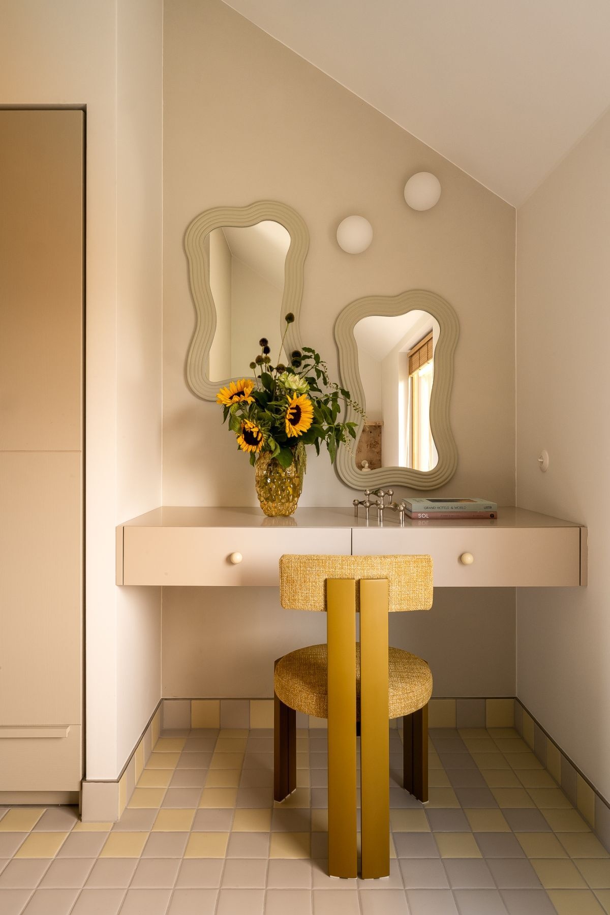 Contemporary bedroom with a poplar burl wood headboard, soft yellow accents, mirrored wall, custom floating dressing table, sculptural yellow chair, and two wavy decorative mirrors.