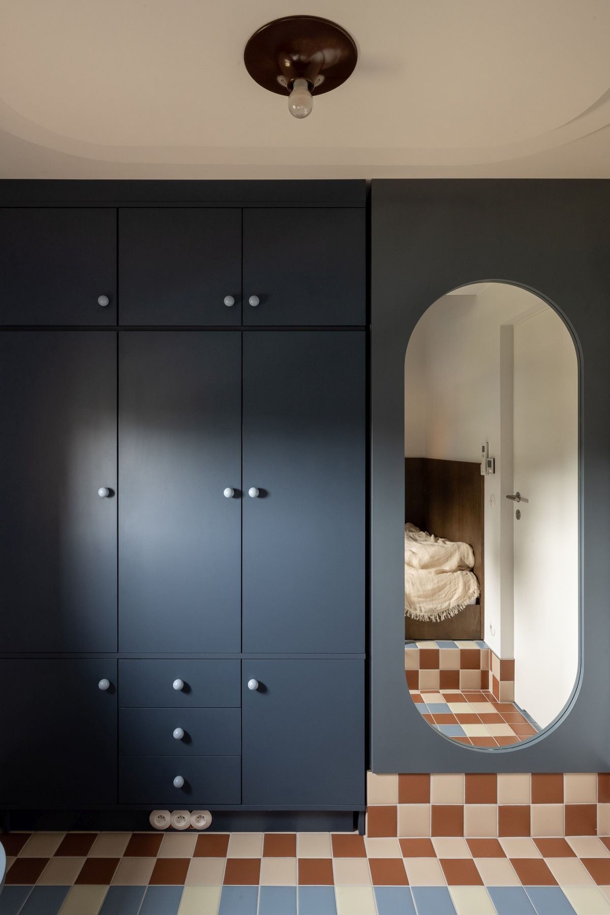 Contemporary bedroom featuring a custom wooden bed, dark blue-gray built-in wardrobes, an oval mirror, and a large upholstered window seat overlooking the outdoor swimming pool.