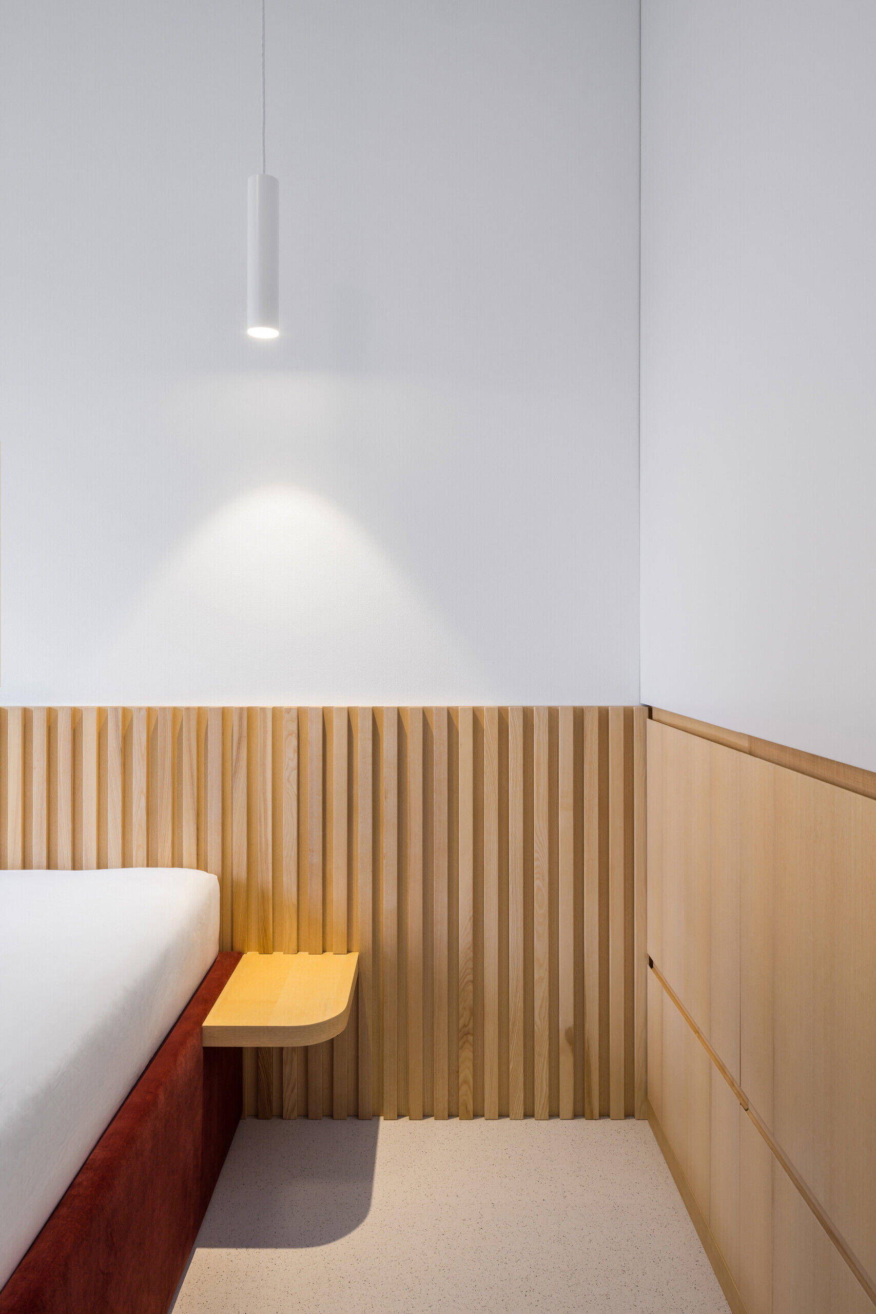 Natural wood finishes and a red upholstered bed frame bring warmth and color to the minimalist interiors.